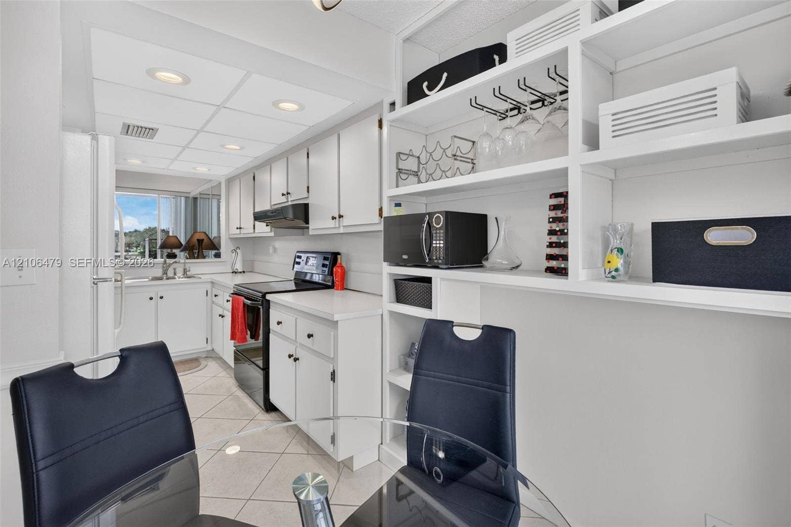 2800 SW 87th Avenue, #1113, Davie, FL 33328 Kitchen featuring white shaker-style cabinetry, solid-surface countertops, tile flooring, recessed lighting, and built-in open display shelving