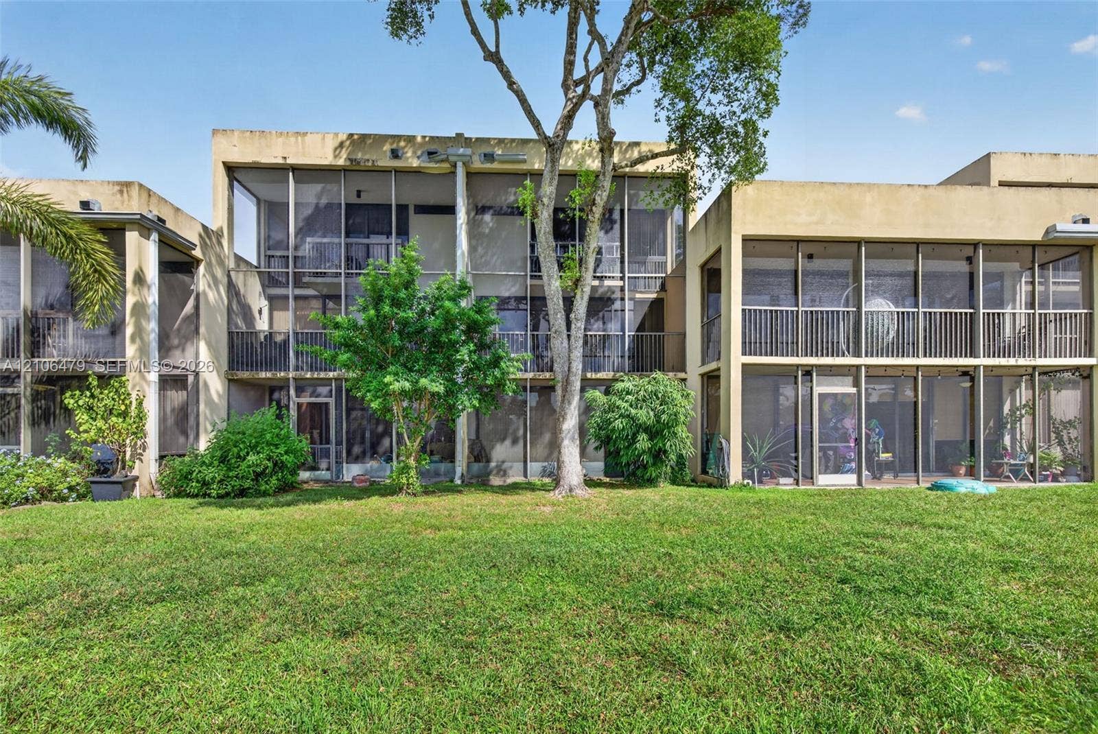 2800 SW 87th Avenue, #1113, Davie, FL 33328 Exterior facade featuring multi-level screened-in lanais, metal railing systems, flat roof architecture, and an expansive lawn with mature landscaping