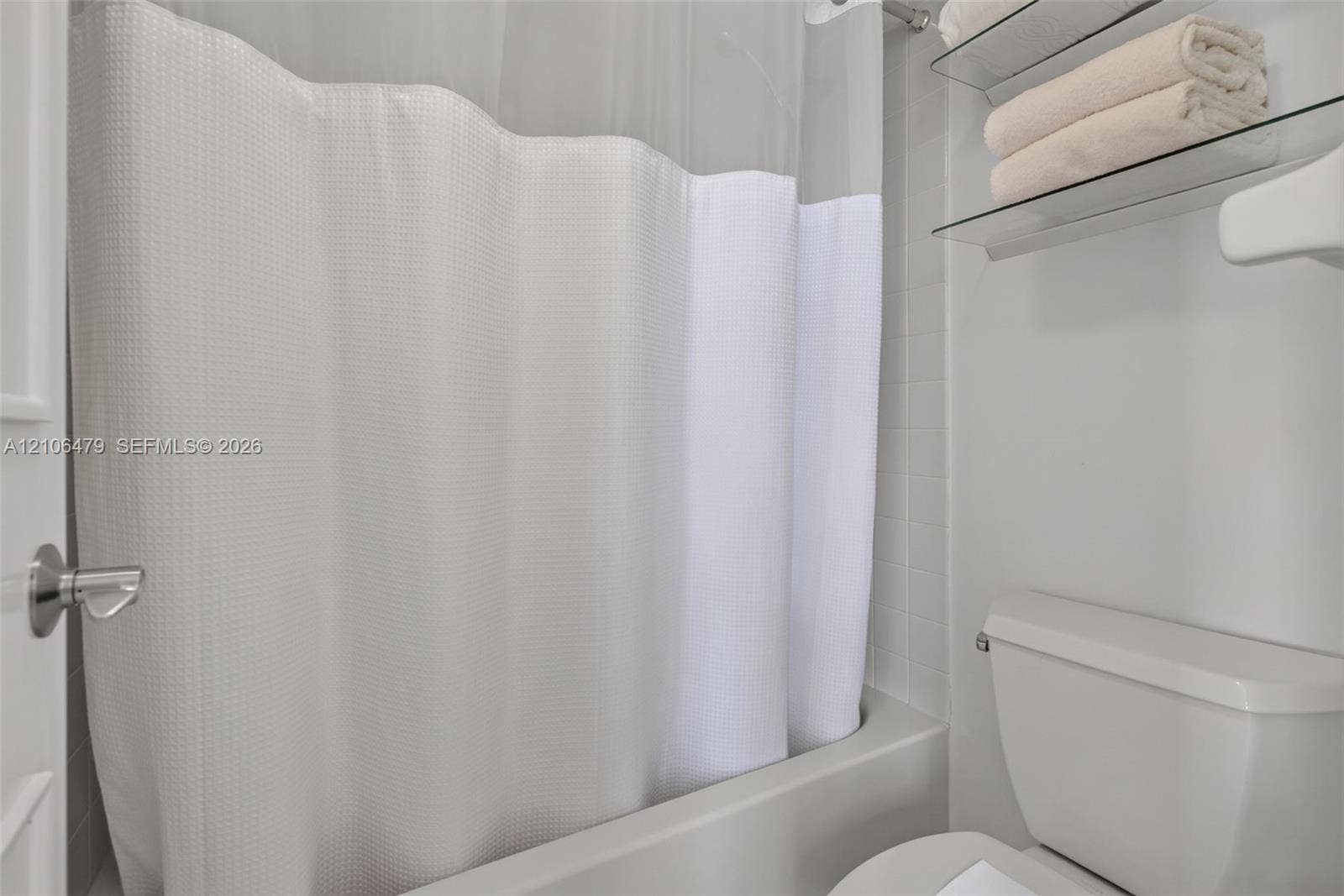 2800 SW 87th Avenue, #1113, Davie, FL 33328 Bathroom featuring a white bathtub, tiled shower surround, dual glass shelving unit, and standard toilet