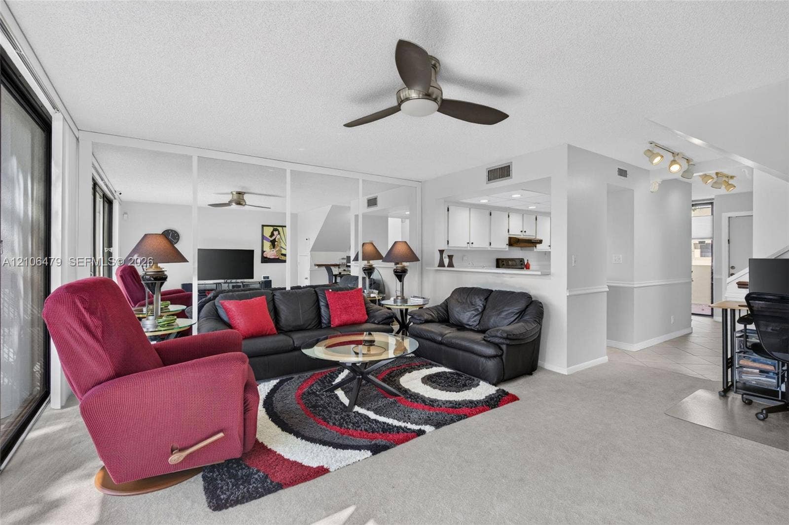 2800 SW 87th Avenue, #1113, Davie, FL 33328 Living area featuring a ceiling fan, wall-to-wall mirrored panels, carpeted flooring, and a pass-through opening to the kitchen
