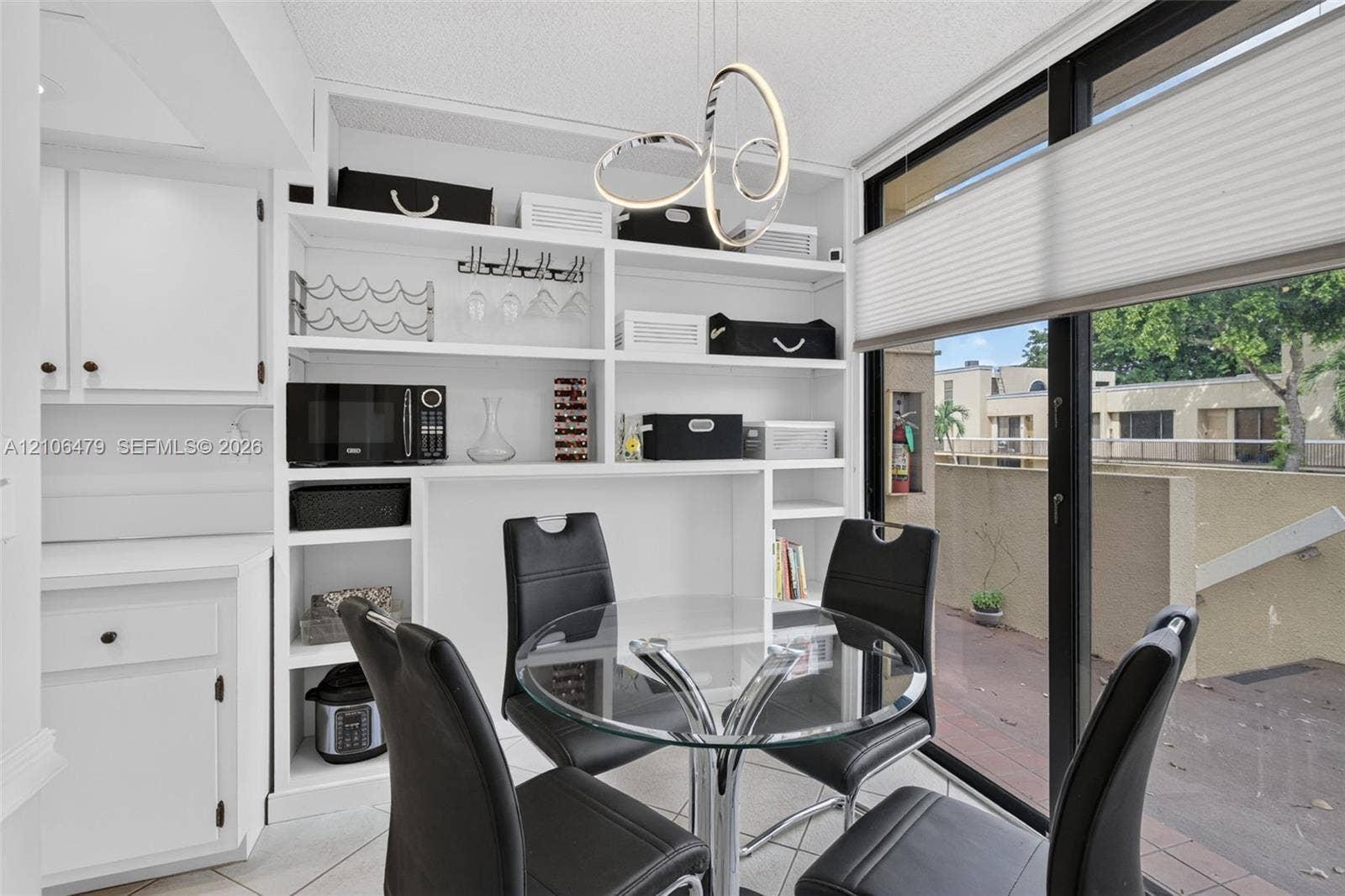2800 SW 87th Avenue, #1113, Davie, FL 33328 Built-in floor-to-ceiling white shelving unit, contemporary sculptural pendant light fixture, and sliding glass door with integrated cellular shades