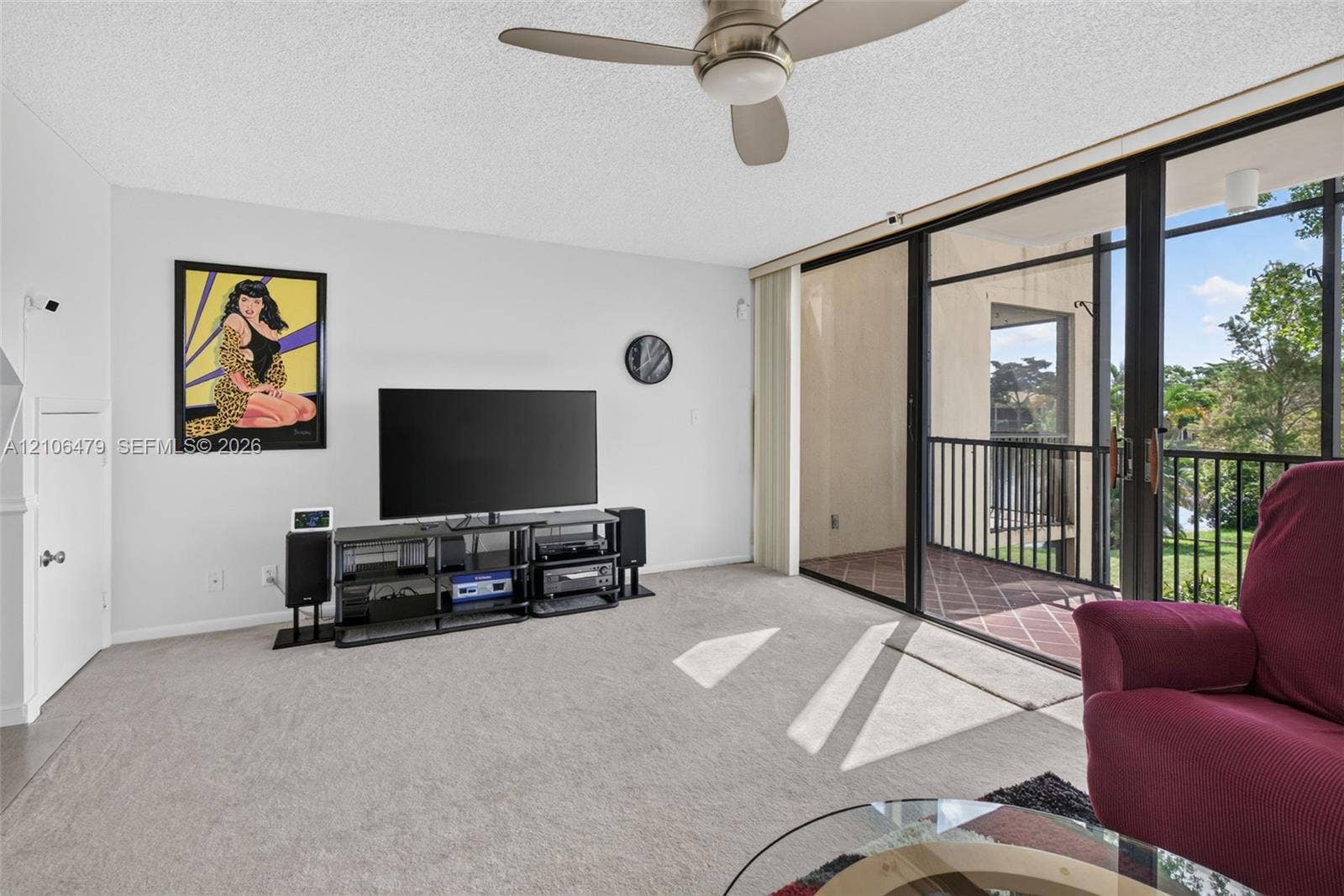 2800 SW 87th Avenue, #1113, Davie, FL 33328 Living area featuring wall-to-wall carpeting, a ceiling-mounted fan, and floor-to-ceiling sliding glass doors providing access to a screened-in balcony with tile flooring and metal railings