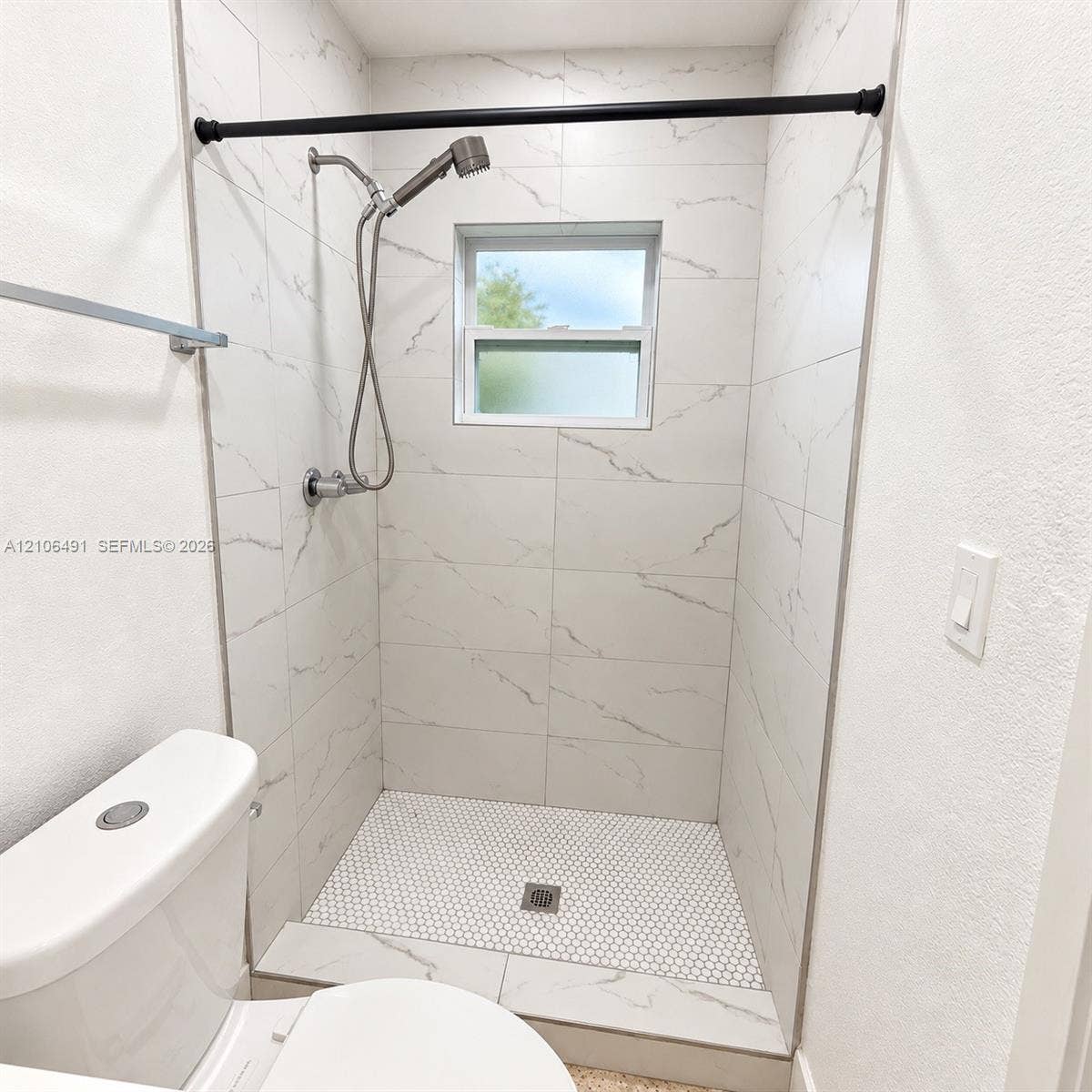 Walk-in shower featuring large-format stone-pattern wall tile, circular mosaic floor tile, hand-held shower fixture, and a built-in window