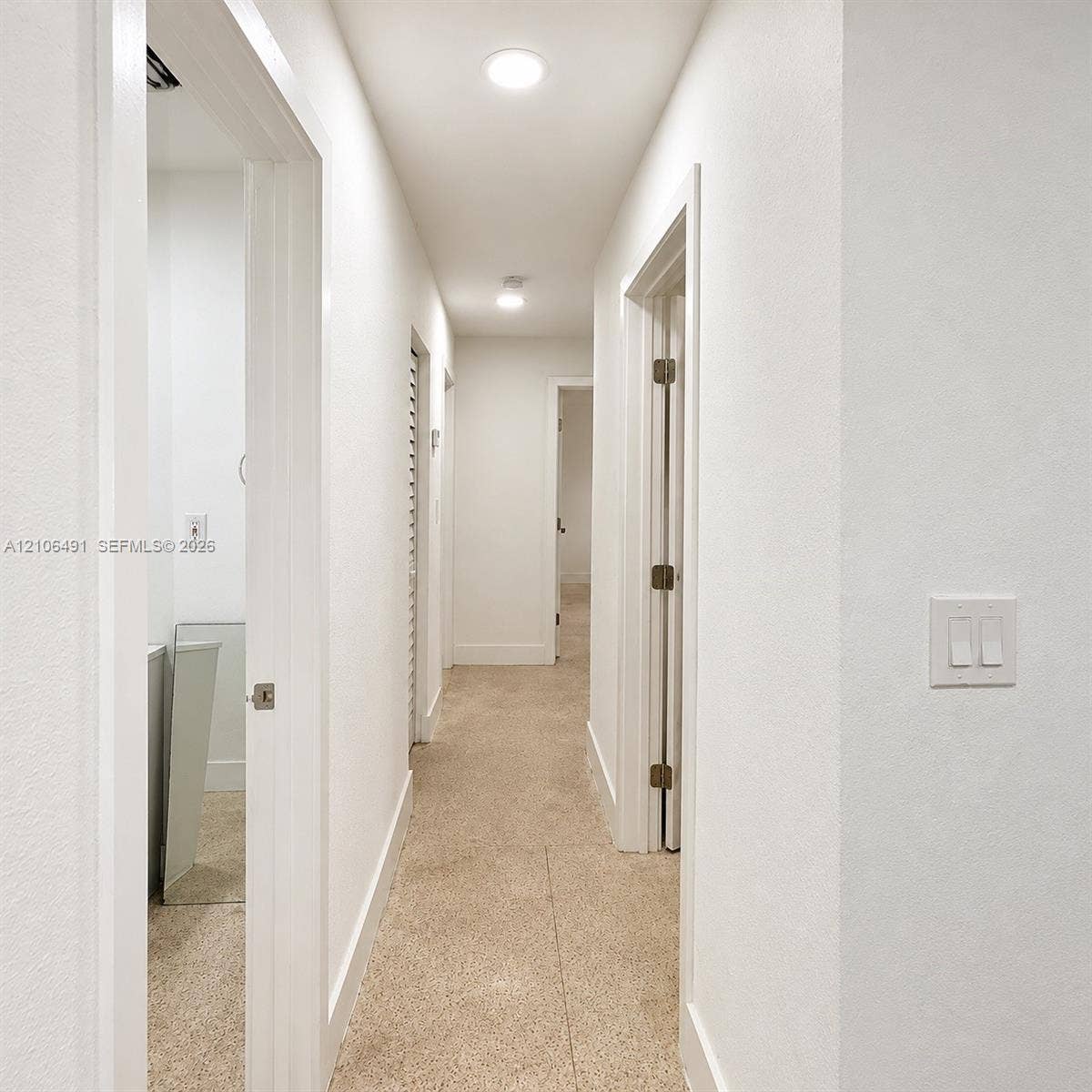 Hallway featuring neutral-toned carpeting, crisp white wall finishes, recessed ceiling lighting, and louvered closet doors