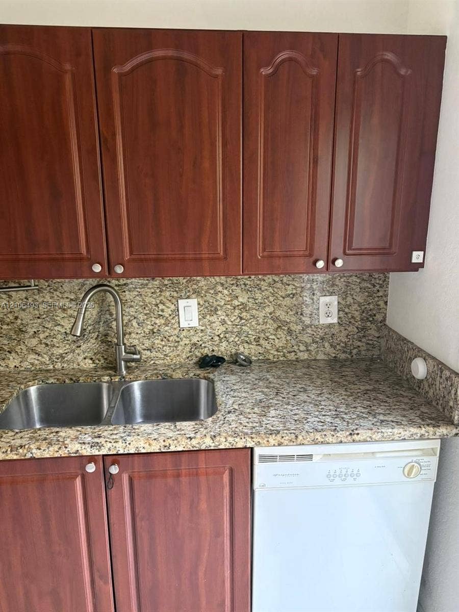 117 SE 3rd Avenue, #7, Hallandale Beach, FL 33009 Kitchen featuring arched-panel wood cabinetry, stone-surface countertops, matching stone backsplash, dual-basin stainless steel sink with high-arc faucet, and built-in dishwasher
