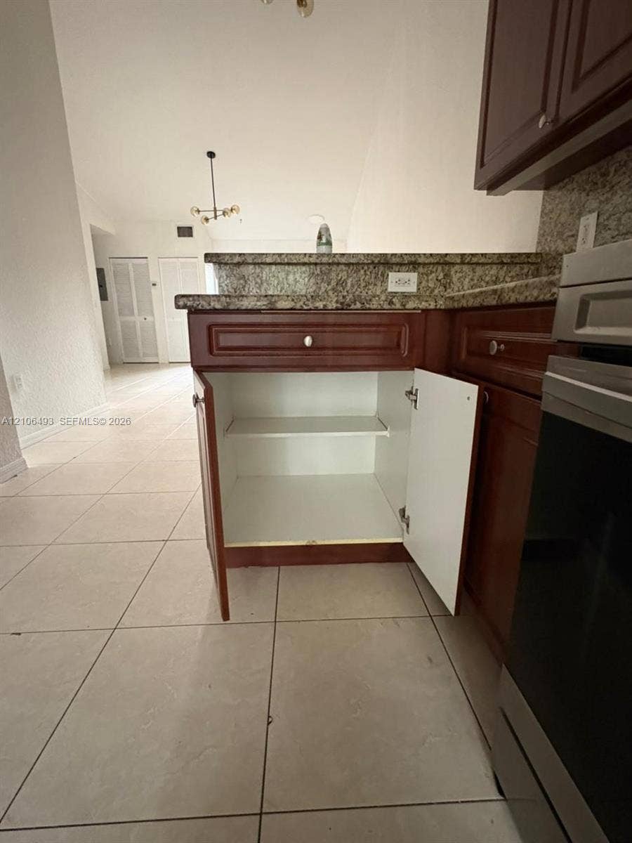 117 SE 3rd Avenue, #7, Hallandale Beach, FL 33009 Kitchen featuring cabinetry with a dark wood finish, stone-surfaced countertops, and neutral-toned tile flooring