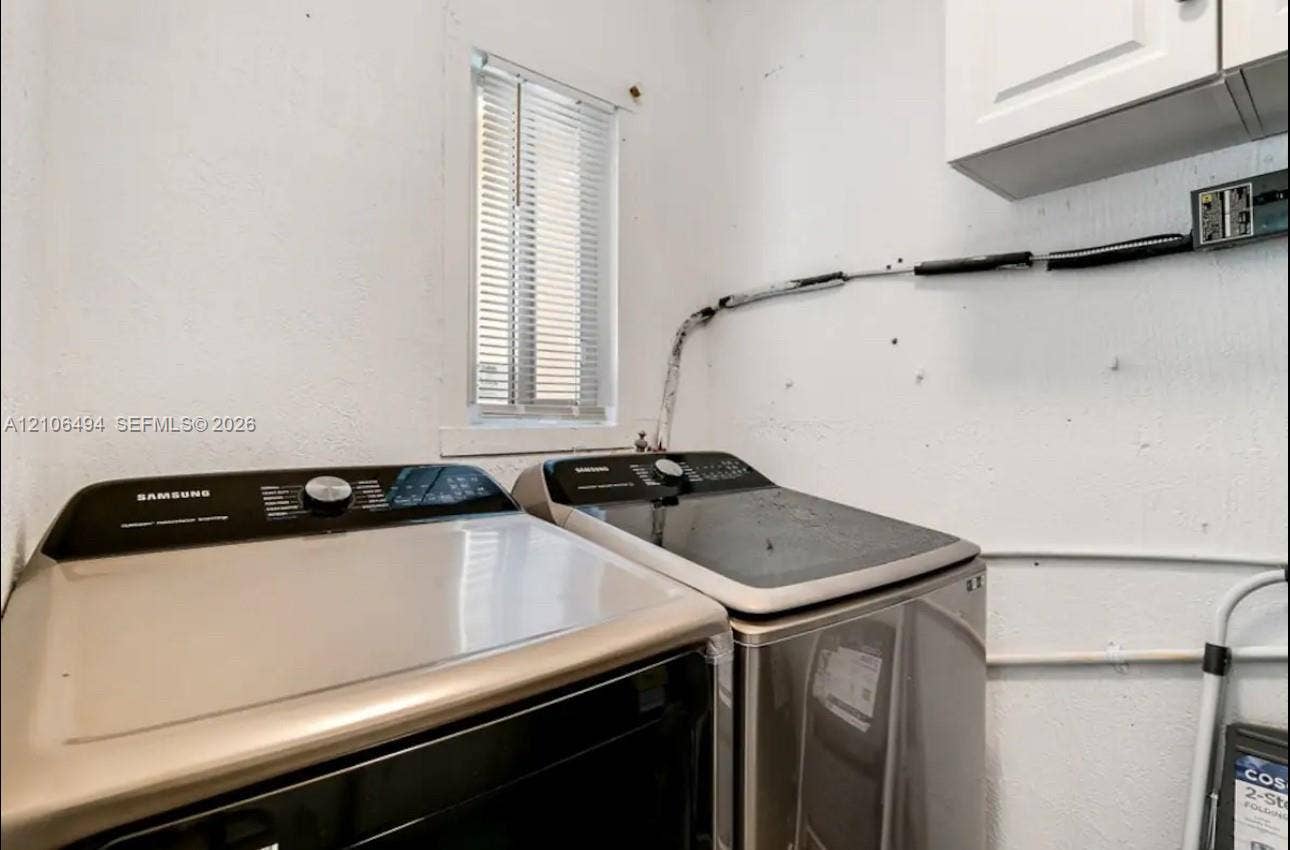 Utility room featuring wall-mounted white cabinetry and an operable window with horizontal blinds