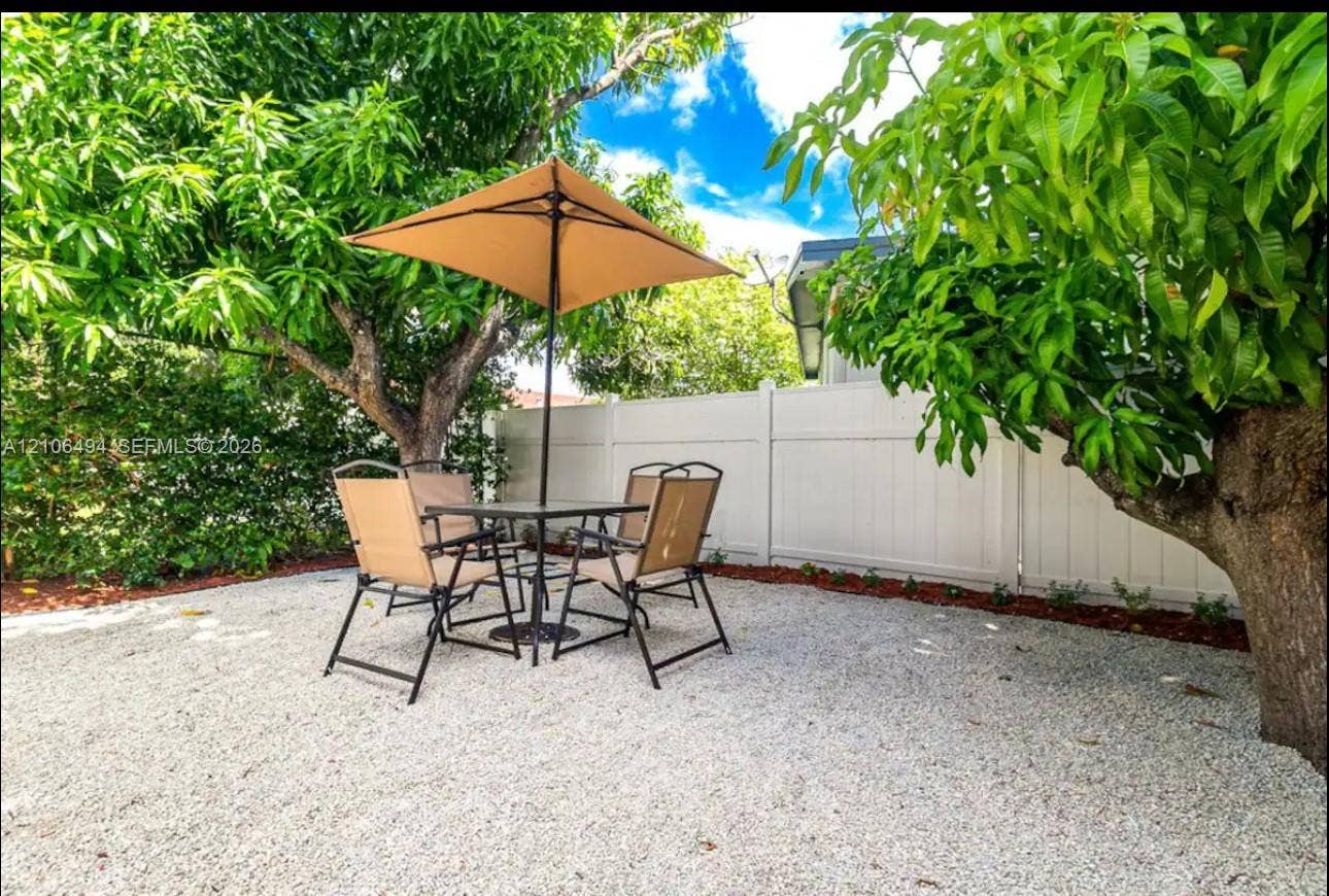 Backyard featuring stone ground cover, perimeter vinyl fencing, and mature canopy trees