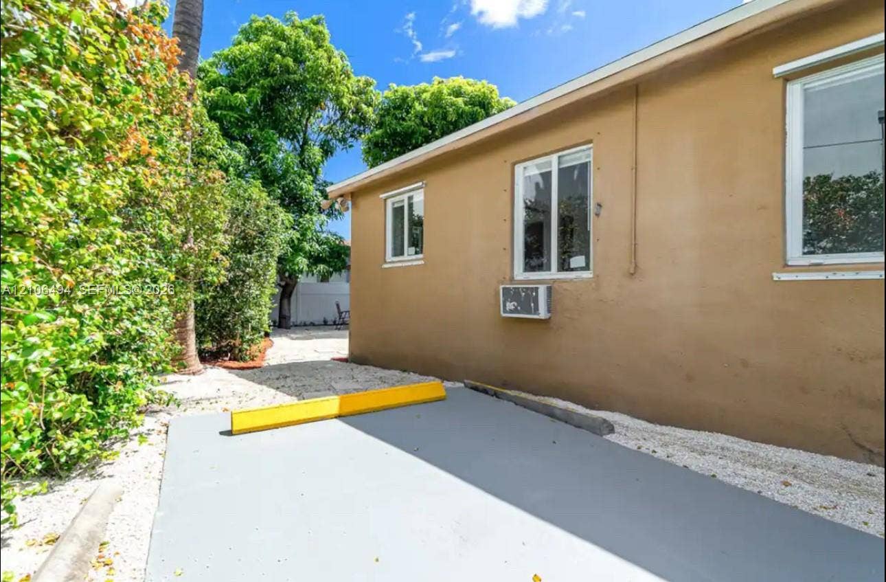 Stucco exterior featuring dual-pane windows, a dedicated paved parking area, and surrounding mature landscaping