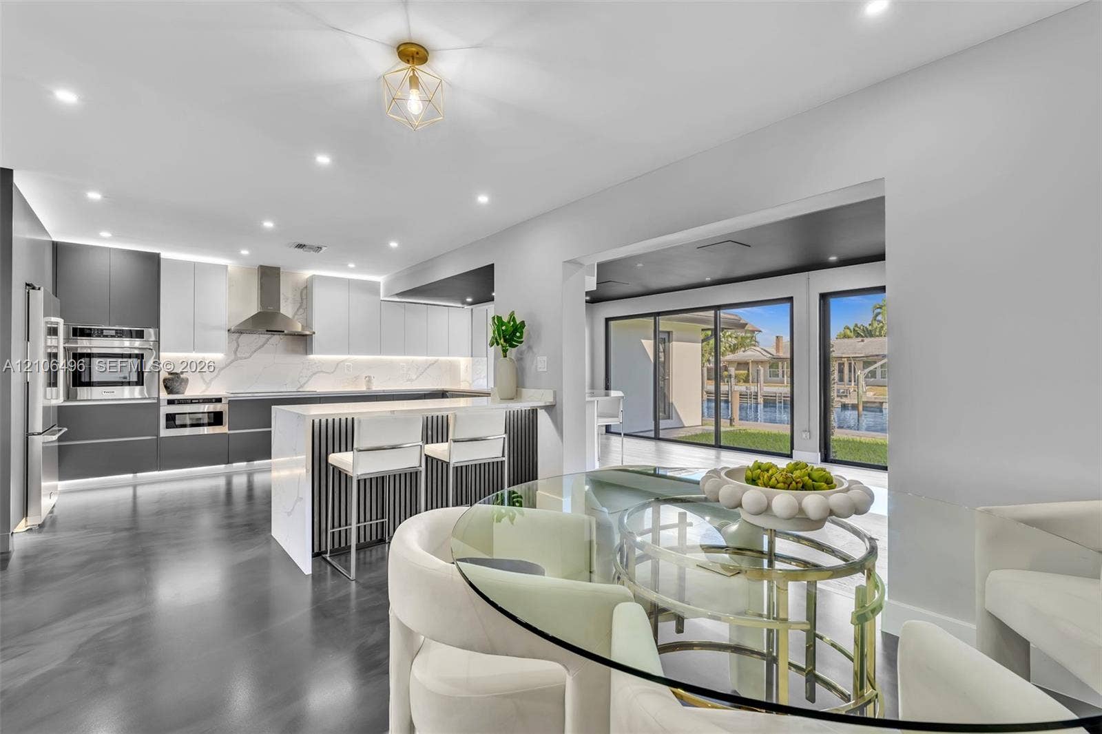 Contemporary kitchen featuring two-toned cabinetry, quartz countertops with full-height backsplash, stainless steel appliances, a tiered center island with vertical slat detailing, and floor-to-ceiling sliding glass doors