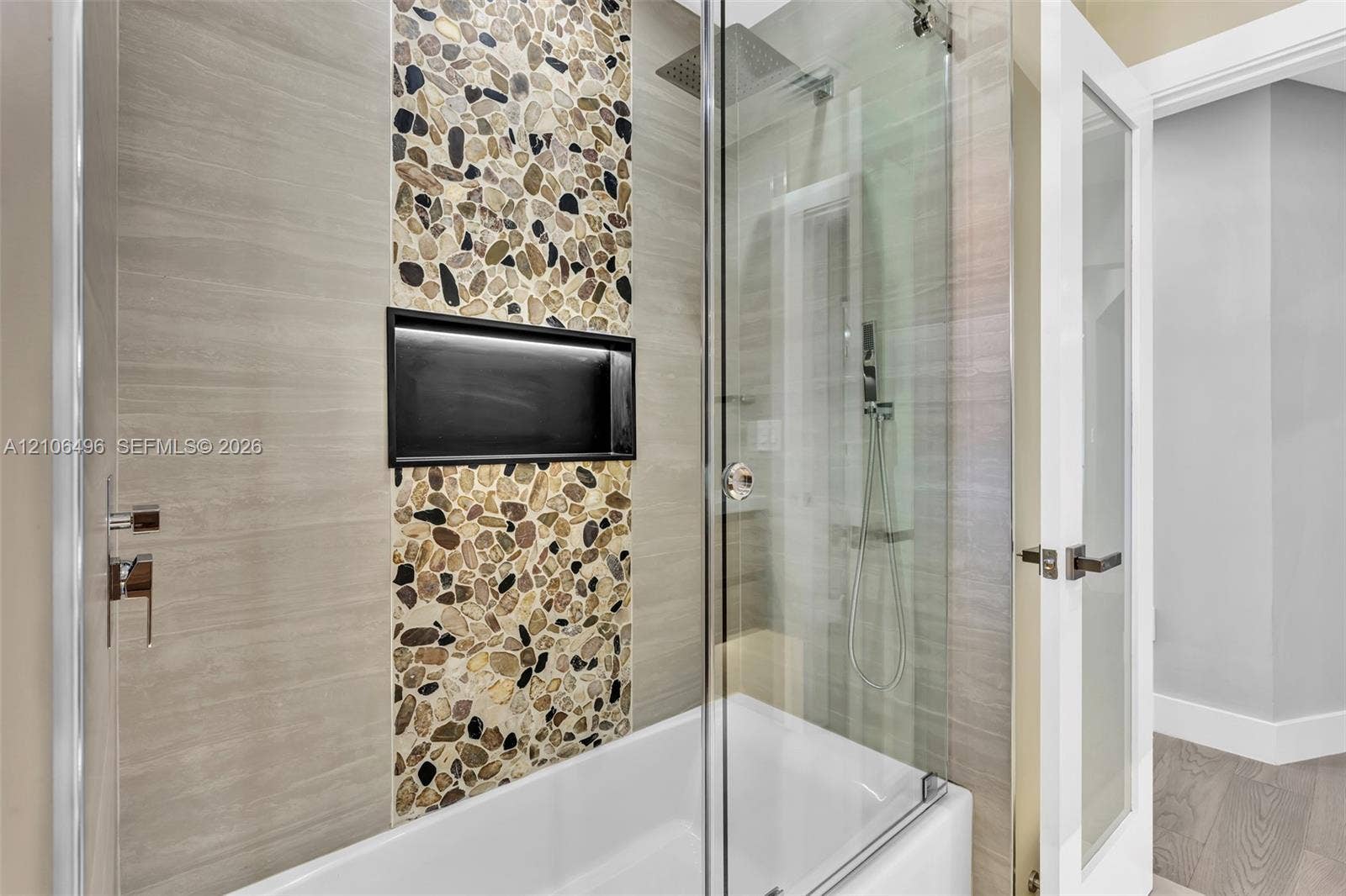 Shower and tub combination featuring horizontal tile surrounds, a decorative vertical pebble-tile inlay, integrated black-framed shower niche, glass shower screen, and rainfall showerhead