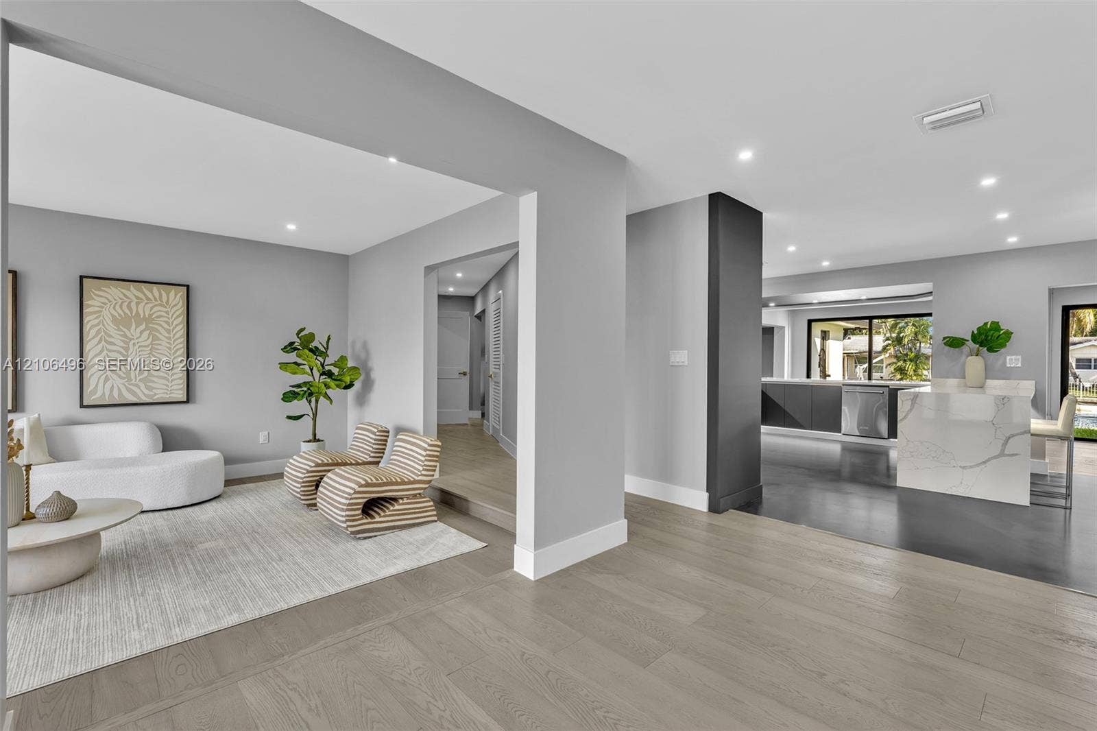 Open-concept floor plan featuring wood-finish flooring, recessed lighting, a stone-surfaced kitchen island, and a dark-toned accent pillar