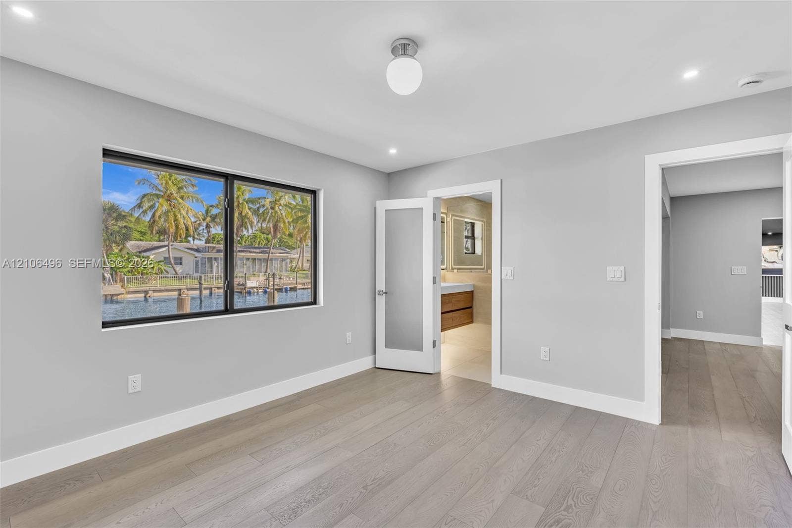 Interior space featuring wood-finish flooring, recessed lighting, a globe ceiling fixture, a large horizontal window with black trim, and a frosted glass-paneled interior door