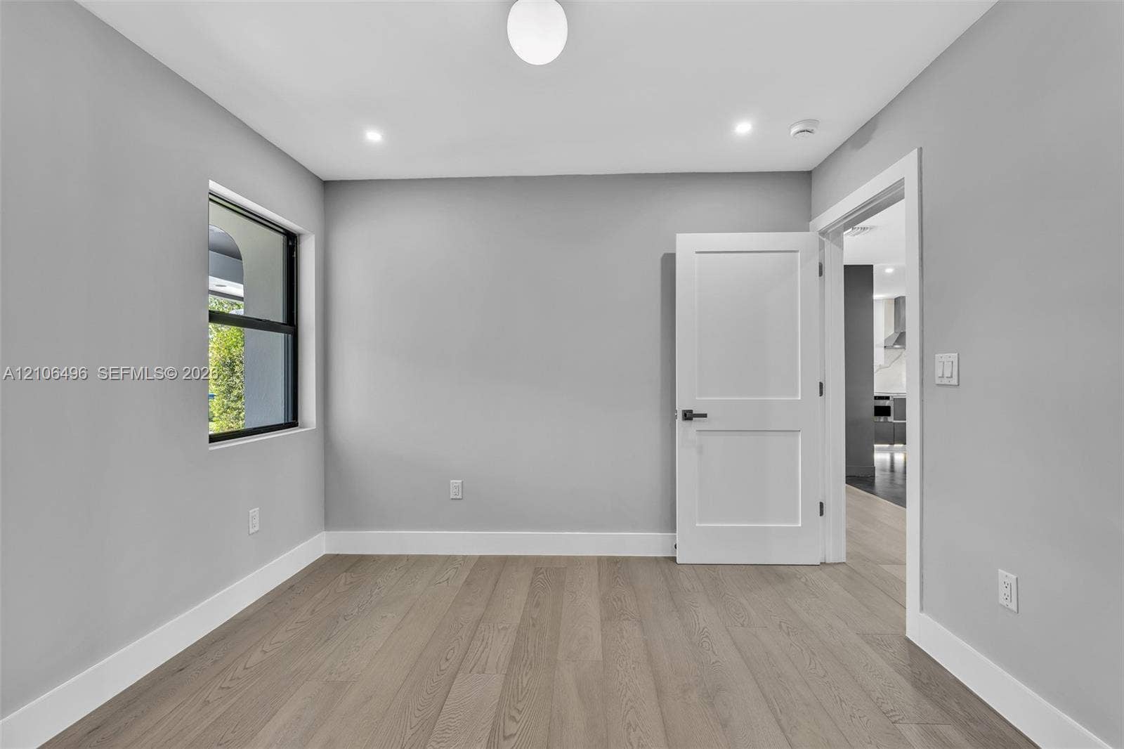 Neutral-toned interior room featuring wood-finish flooring, recessed lighting, a globe flush-mount fixture, a window with a black frame, and a solid-core two-panel interior door