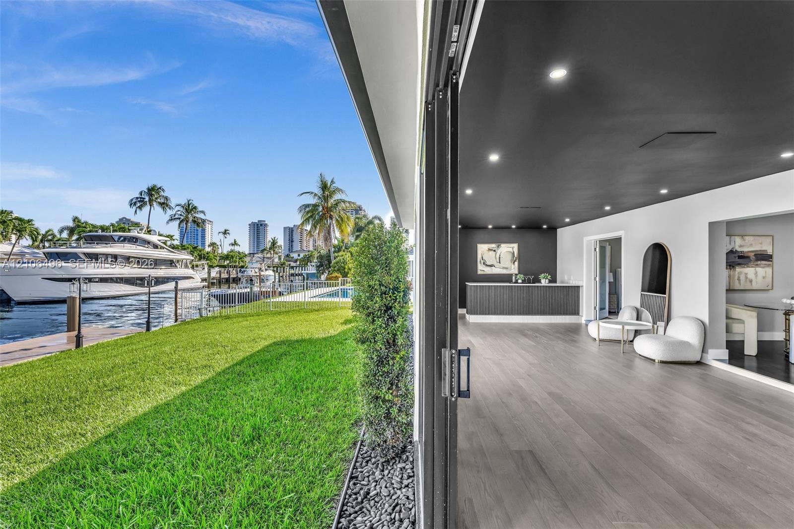 Waterfront property featuring a private boat dock, retractable glass wall system, recessed lighting, wood-finish flooring, and a built-in wet bar