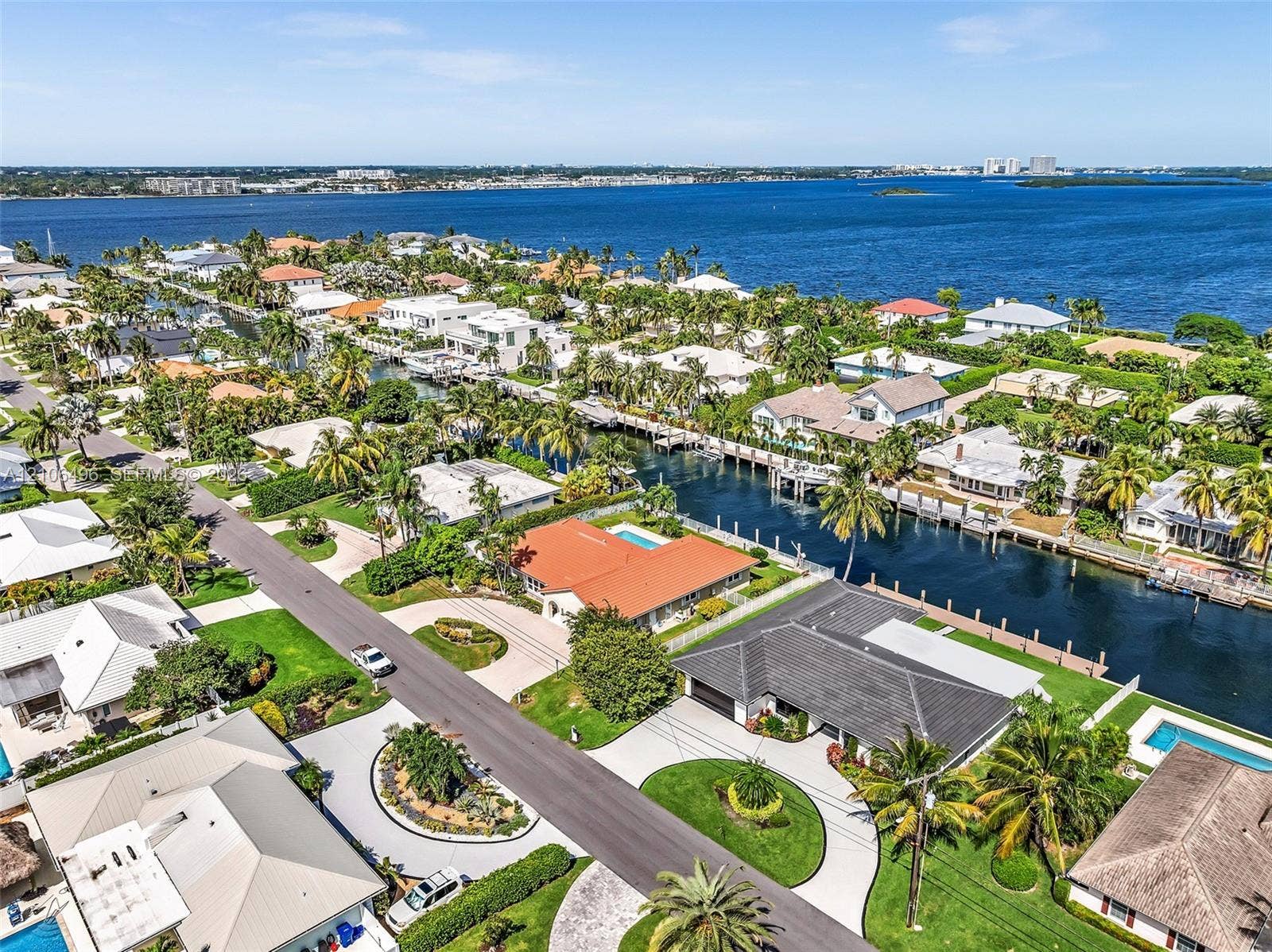 Aerial perspective of a waterfront property featuring a tile roof, paved circular driveway, landscaped lawn, and a private swimming pool