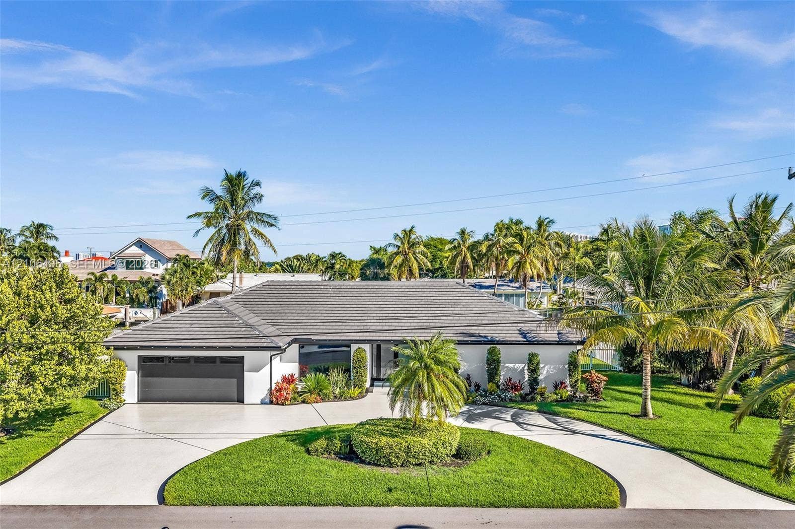 Single-story residence featuring a low-pitched tiled roof, a circular concrete driveway, and an attached two-car garage, complemented by mature tropical landscaping