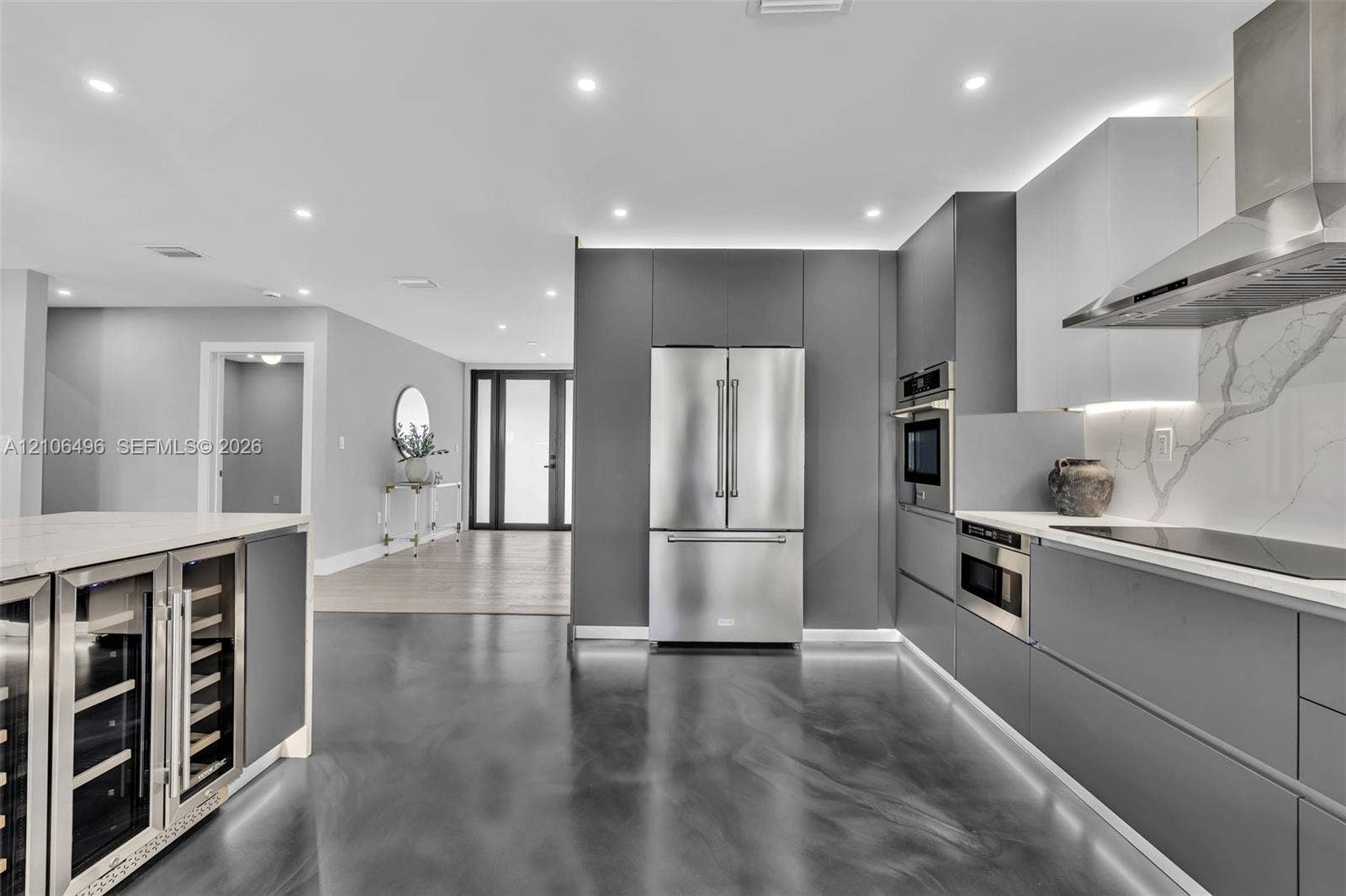 Modern kitchen featuring handleless cabinetry, stainless steel appliances, a built-in wine refrigerator, under-cabinet lighting, and a stone-patterned backsplash