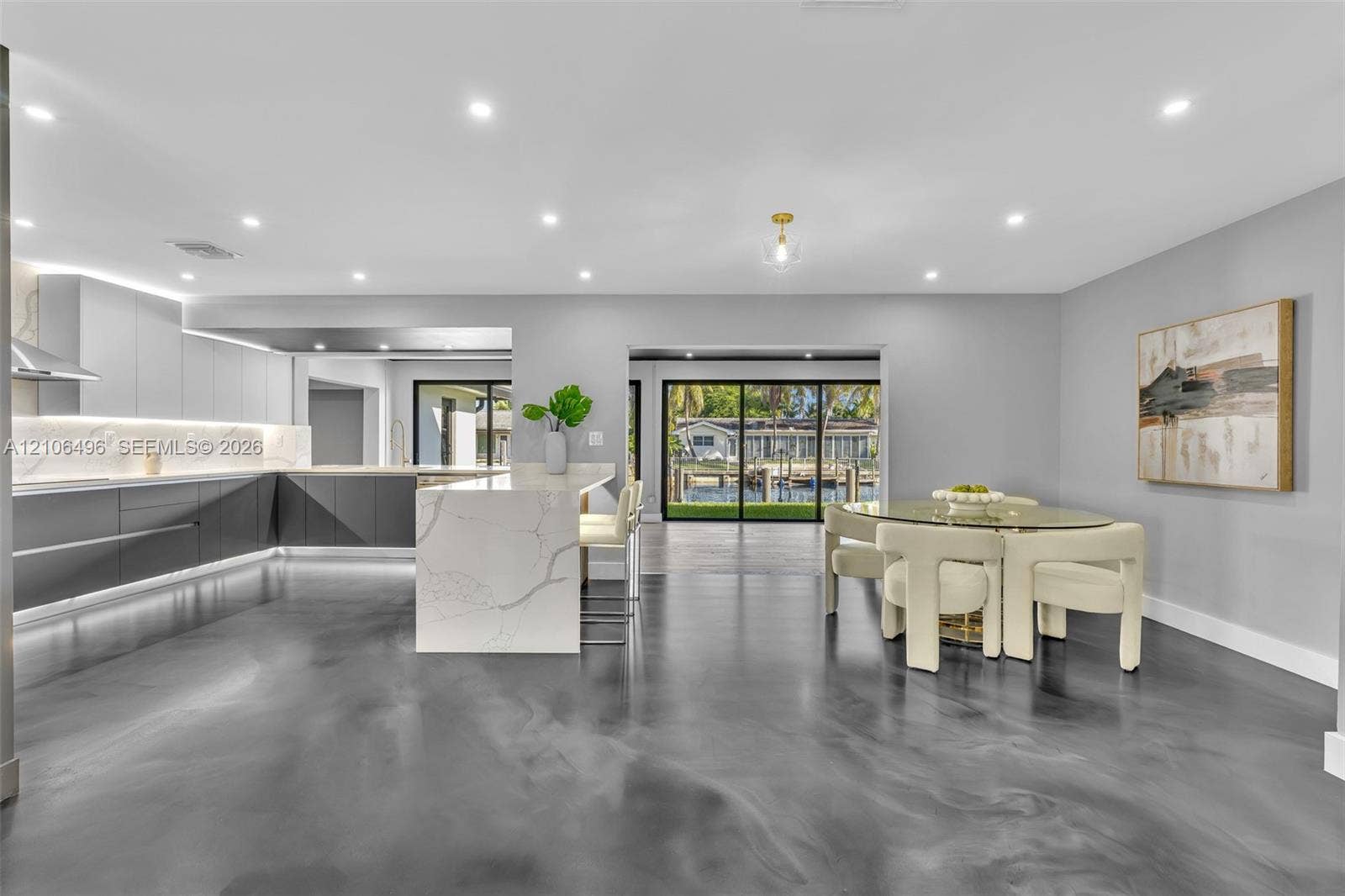 Open-concept kitchen featuring two-toned flat-panel cabinetry, a stone-surface waterfall island, recessed lighting, and sliding glass doors
