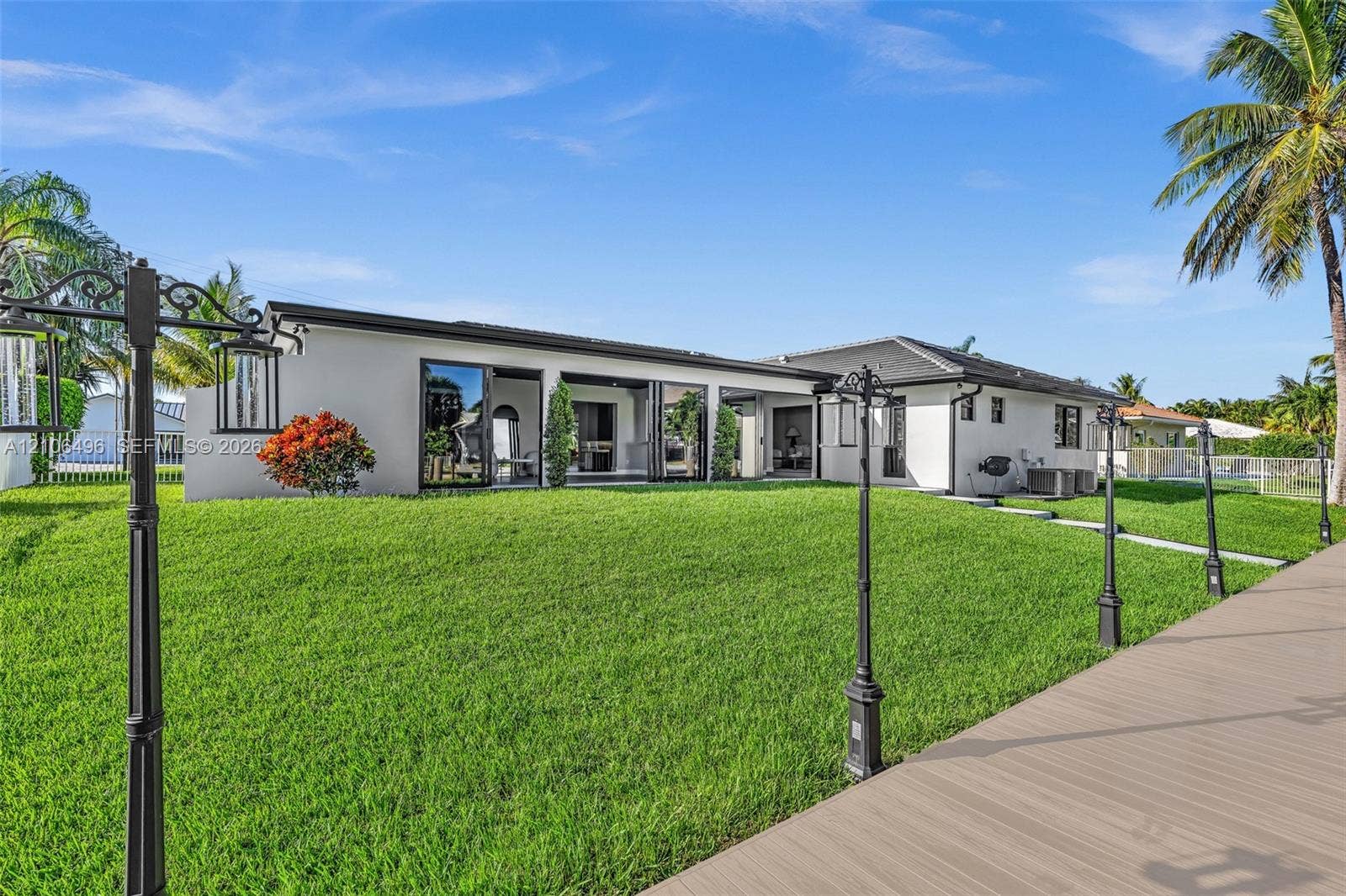Exterior of a single-story residence featuring a smooth stucco facade, multi-panel sliding glass doors, a wide composite deck, and custom post-mounted exterior lighting