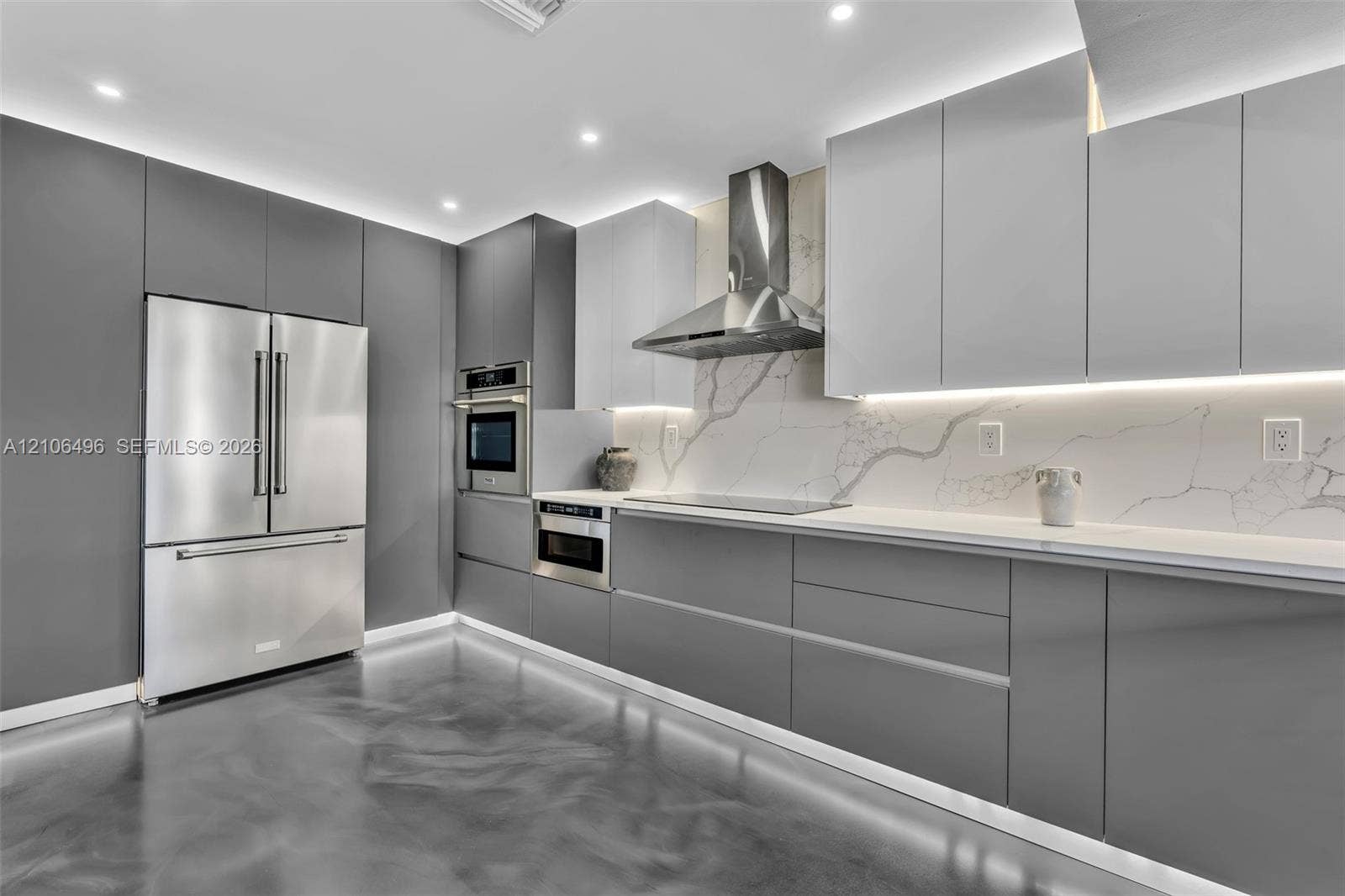 Kitchen featuring floor-to-ceiling cabinetry, stainless steel appliances, stone-surface backsplash, integrated under-cabinet lighting, and polished concrete flooring