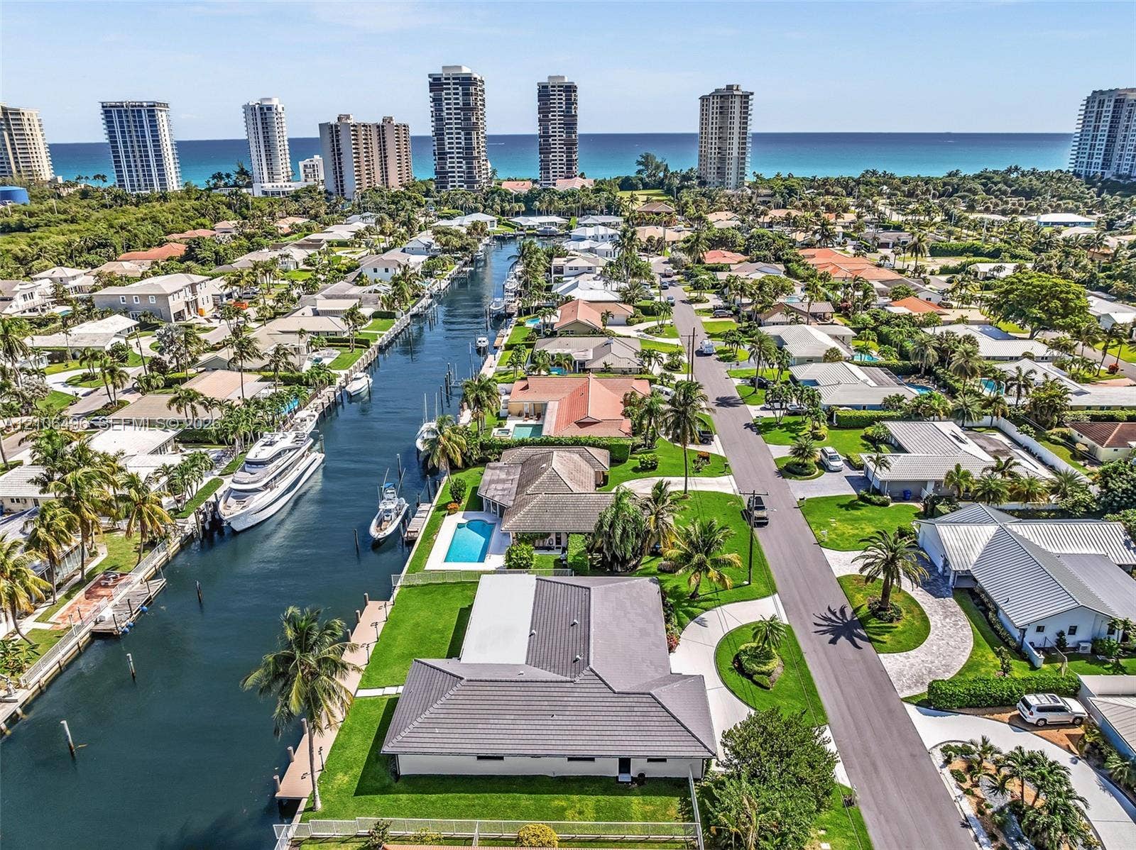 Aerial perspective of a waterfront property featuring direct canal access, a private swimming pool, concrete hardscaping, and mature tropical landscaping