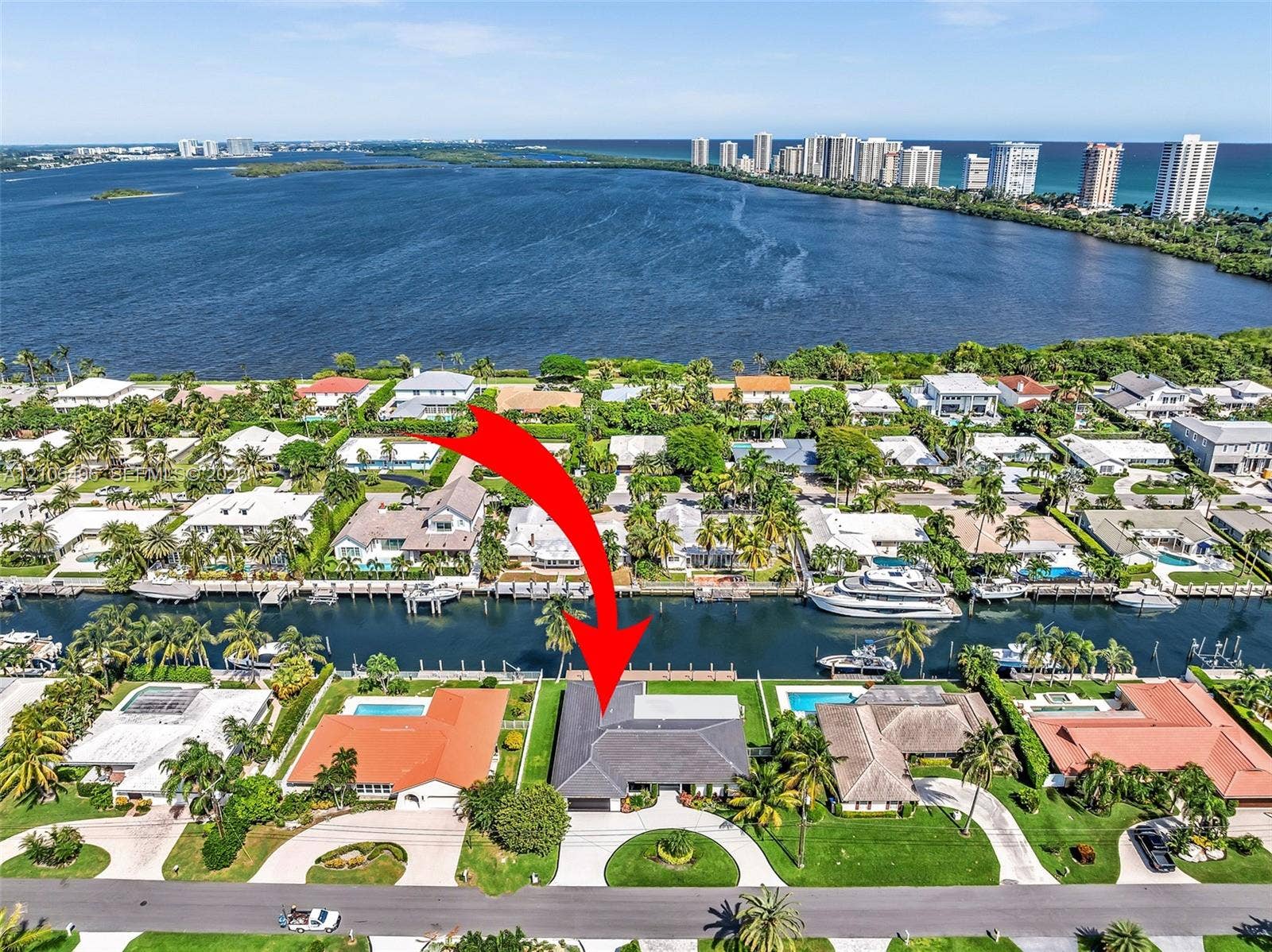 Aerial perspective of a canalfront property featuring a private boat dock, multi-pitched roofline, curved paved driveway, and mature landscaping