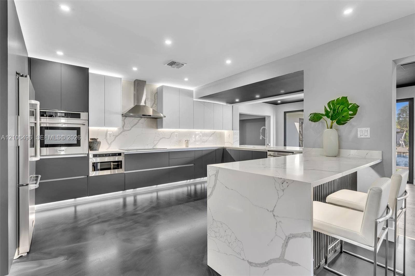 Kitchen featuring two-tone flat-panel cabinetry, a waterfall-edge stone countertop, integrated stainless steel appliances, and under-cabinet accent lighting
