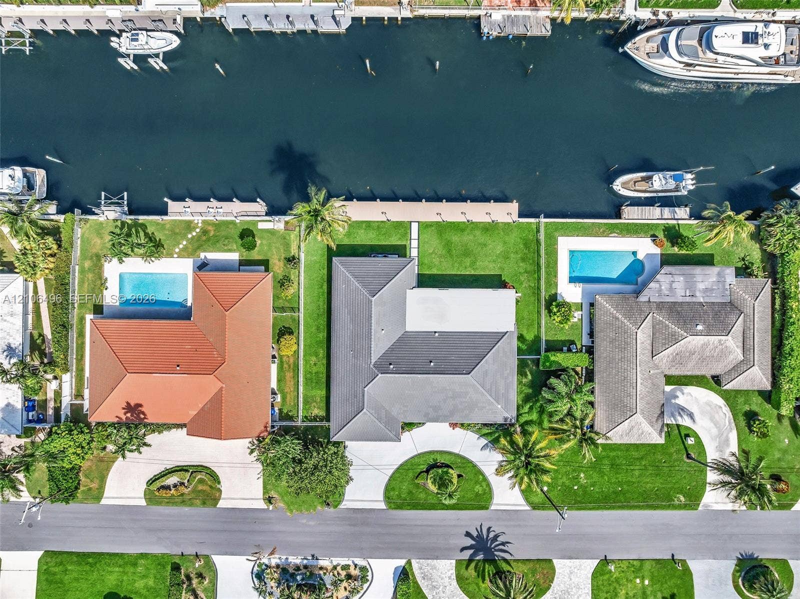 Waterfront property featuring a private boat dock, rectangular swimming pool, manicured lawn, and multi-faceted hipped roofline