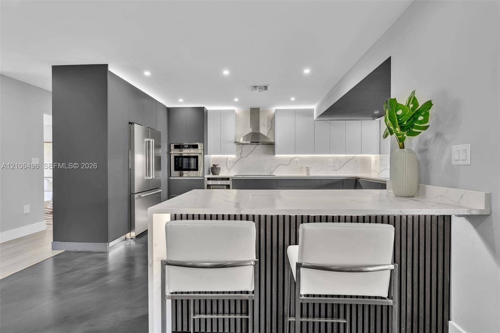 Modern kitchen featuring dual-tone cabinetry, quartz countertops, stainless steel appliances, an island with slatted detailing, and under-cabinet lighting