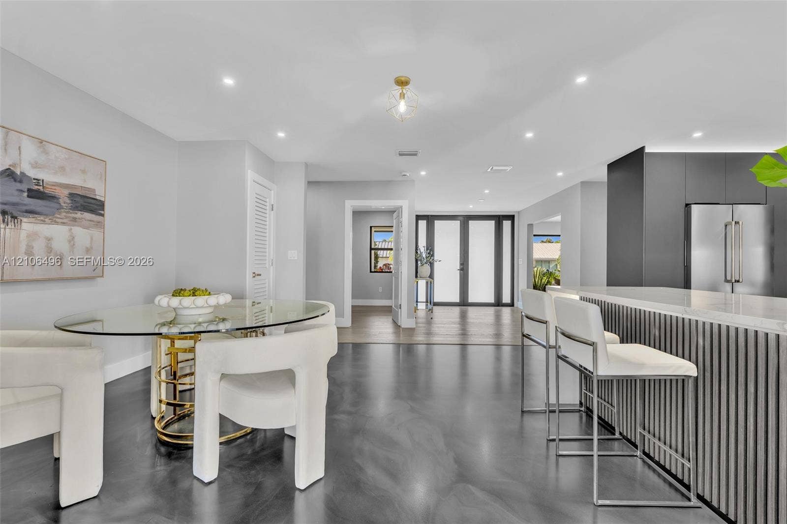 Open-concept interior featuring high-gloss polished flooring, recessed lighting, a modern kitchen island with vertical slat detailing, and a multi-panel glass entry door