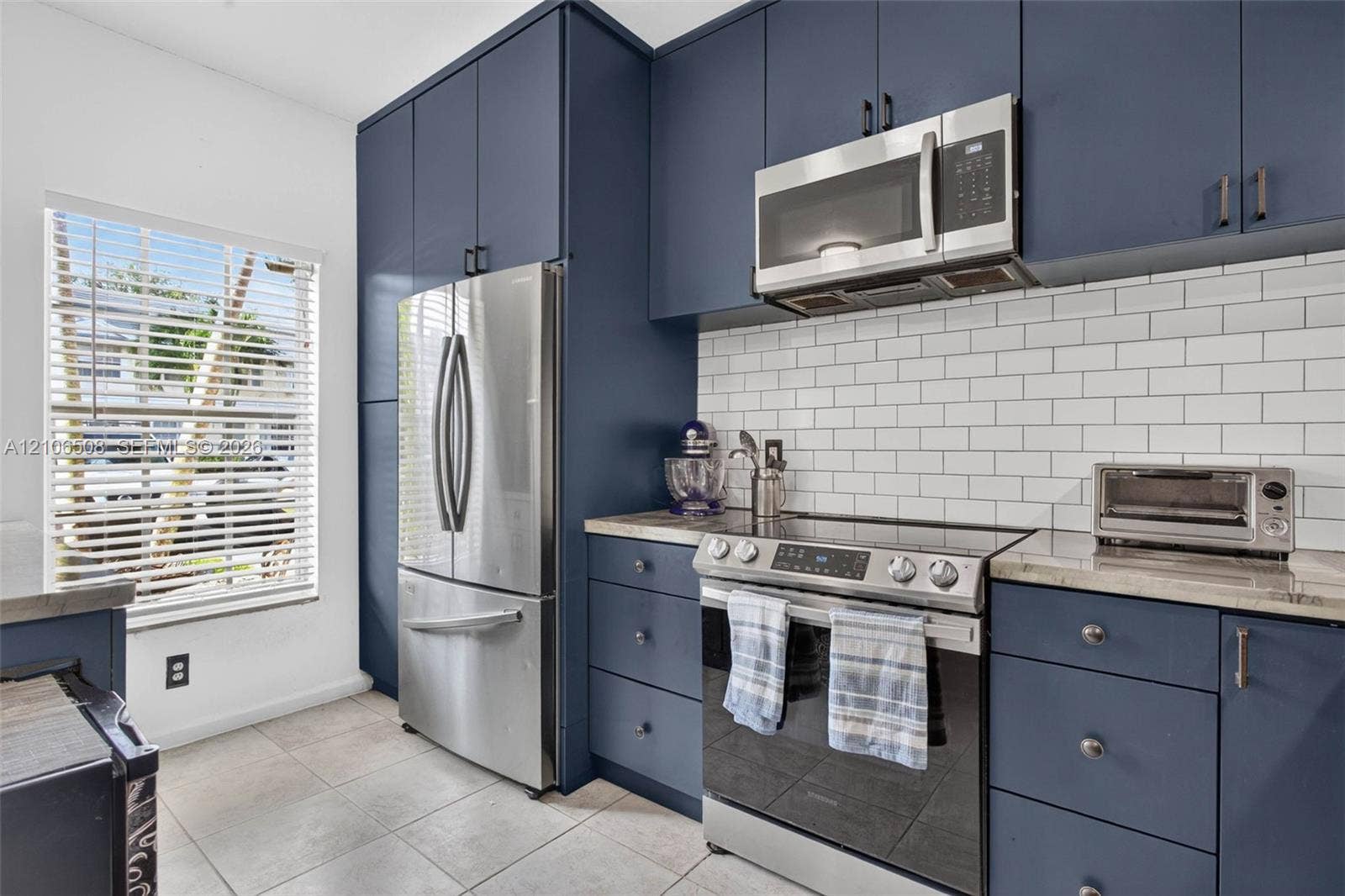 Navy blue cabinetry, stainless steel appliances, white subway tile backsplash, solid surface countertops, and tile flooring