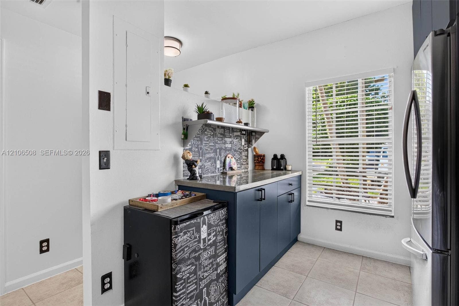 Navy blue base cabinetry, stone-finish countertop, patterned tile backsplash, stainless steel refrigerator, and ceramic tile flooring