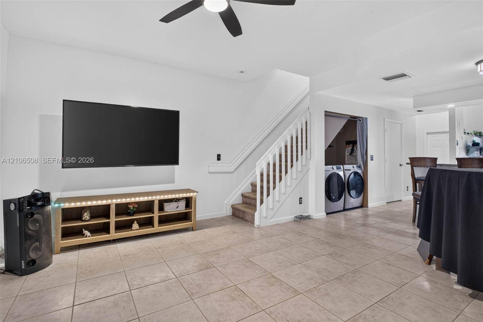 Open-concept area featuring neutral ceramic tile flooring, staircase with white wooden balustrades, recessed lighting, ceiling fan, and dedicated laundry alcove