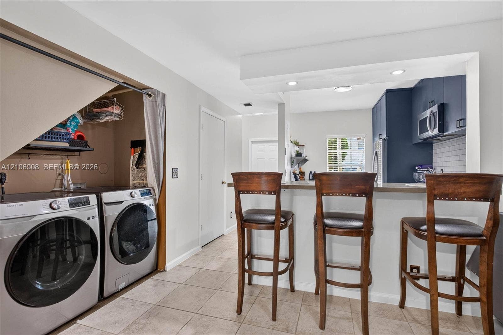 Kitchen featuring a breakfast bar, recessed ceiling lighting, and solid-surface countertops, accompanied by a laundry area with built-in shelving and tile flooring