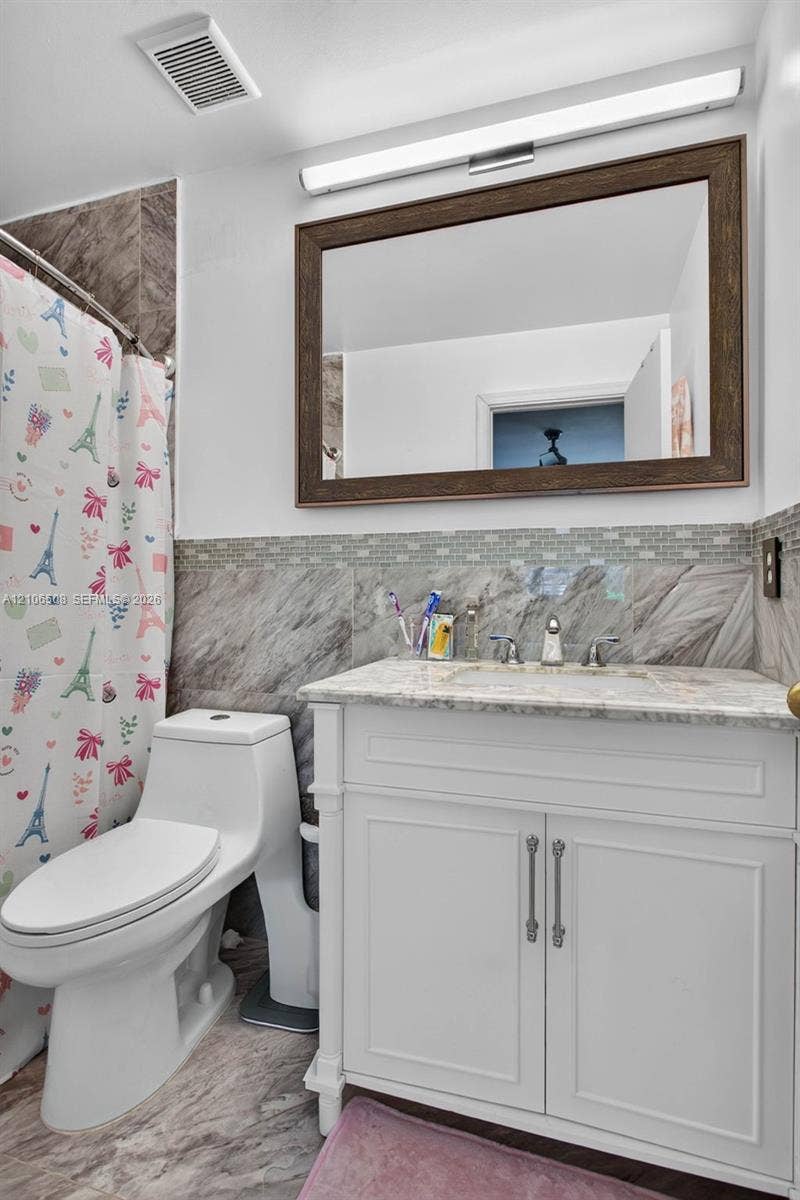 White vanity cabinet with stone countertop and integrated sink, full-width mirror with wood frame, and stone tile wainscoting