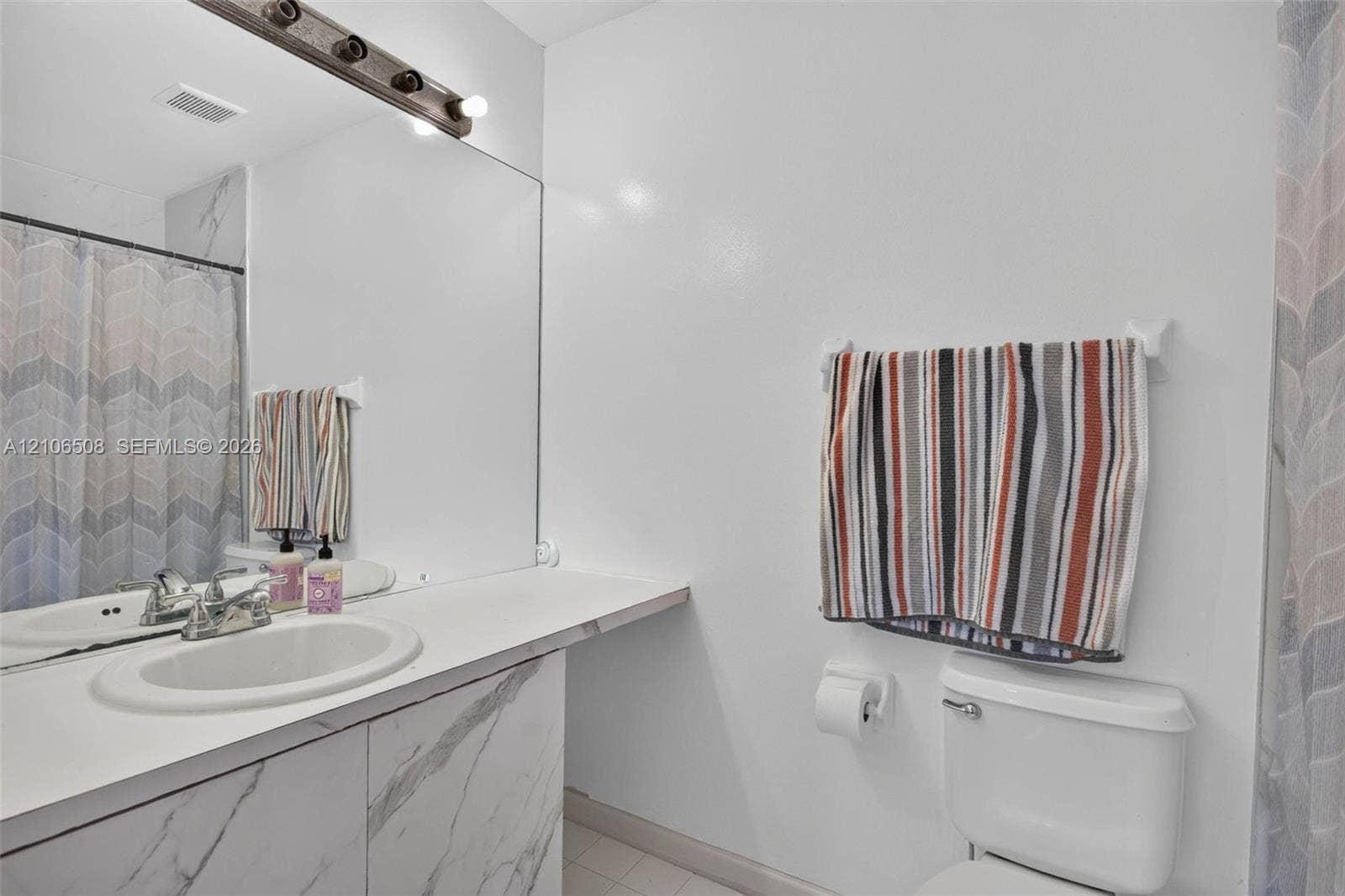 Vanity featuring a stone-finish facade, an integrated sink, an expansive wall-to-wall mirror, and a multi-bulb light fixture
