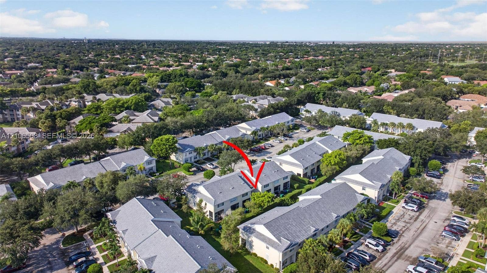 Aerial perspective of multi-family residential structure featuring a pitched shingle roof, light-toned exterior finish, and designated off-street surface parking