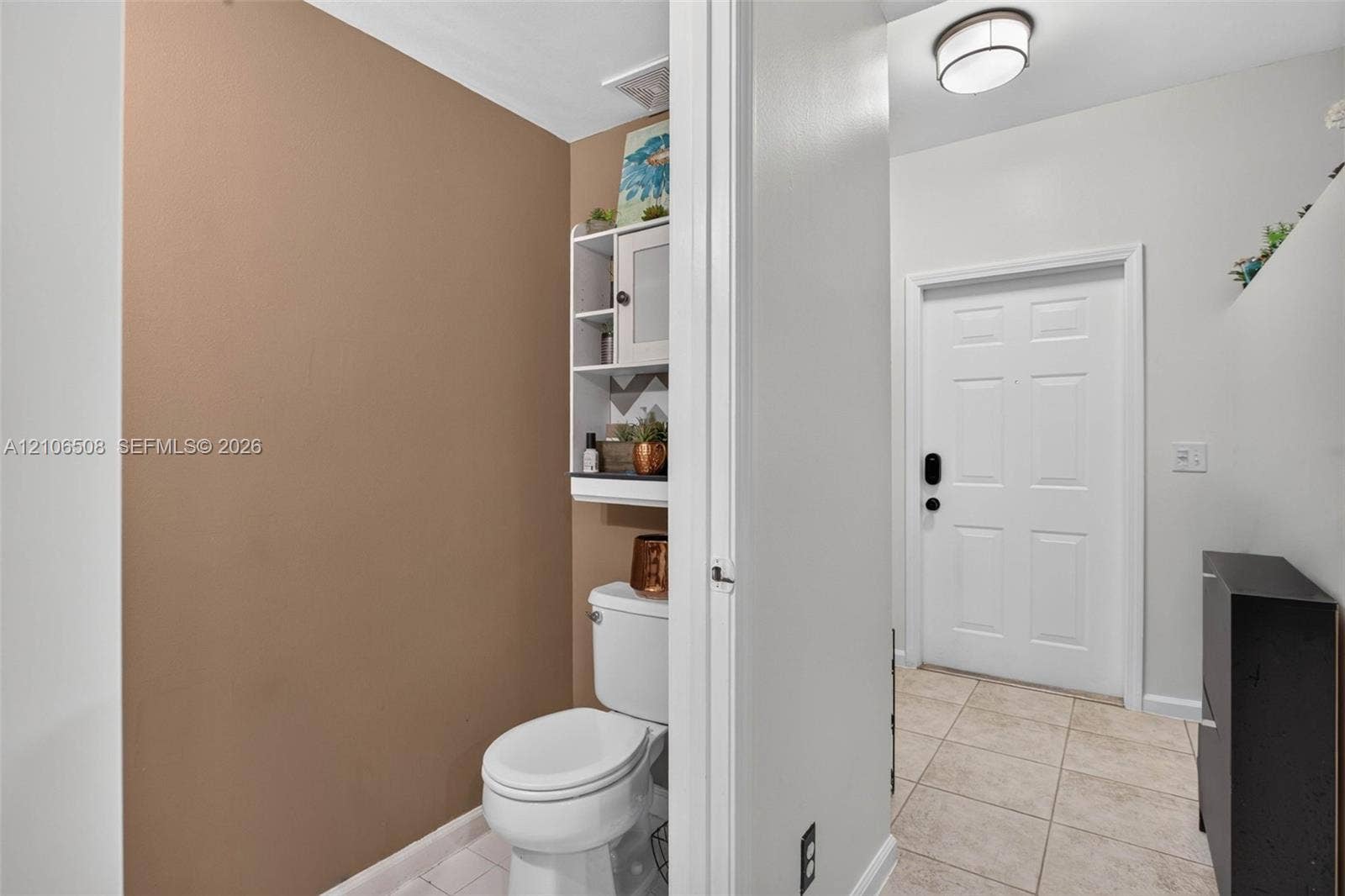 Ceramic tile flooring, white entry door with smart lock, flush-mount ceiling light fixture, and built-in wall shelving