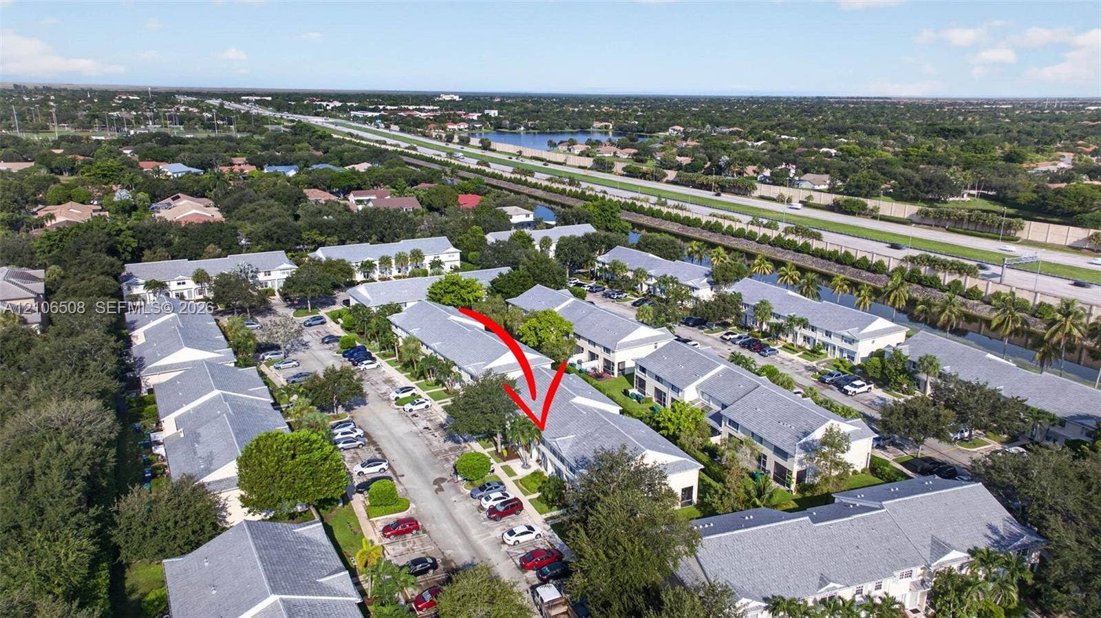 Aerial perspective of multi-family complex featuring light-colored shingled roofing, paved surface parking, and mature landscape elements