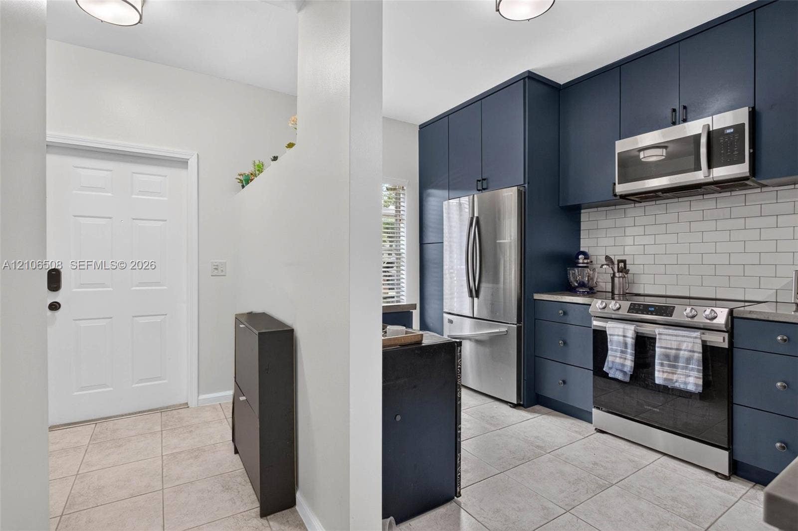 Kitchen featuring dark navy cabinetry, white subway tile backsplash, stainless steel appliances, and large-format tile flooring