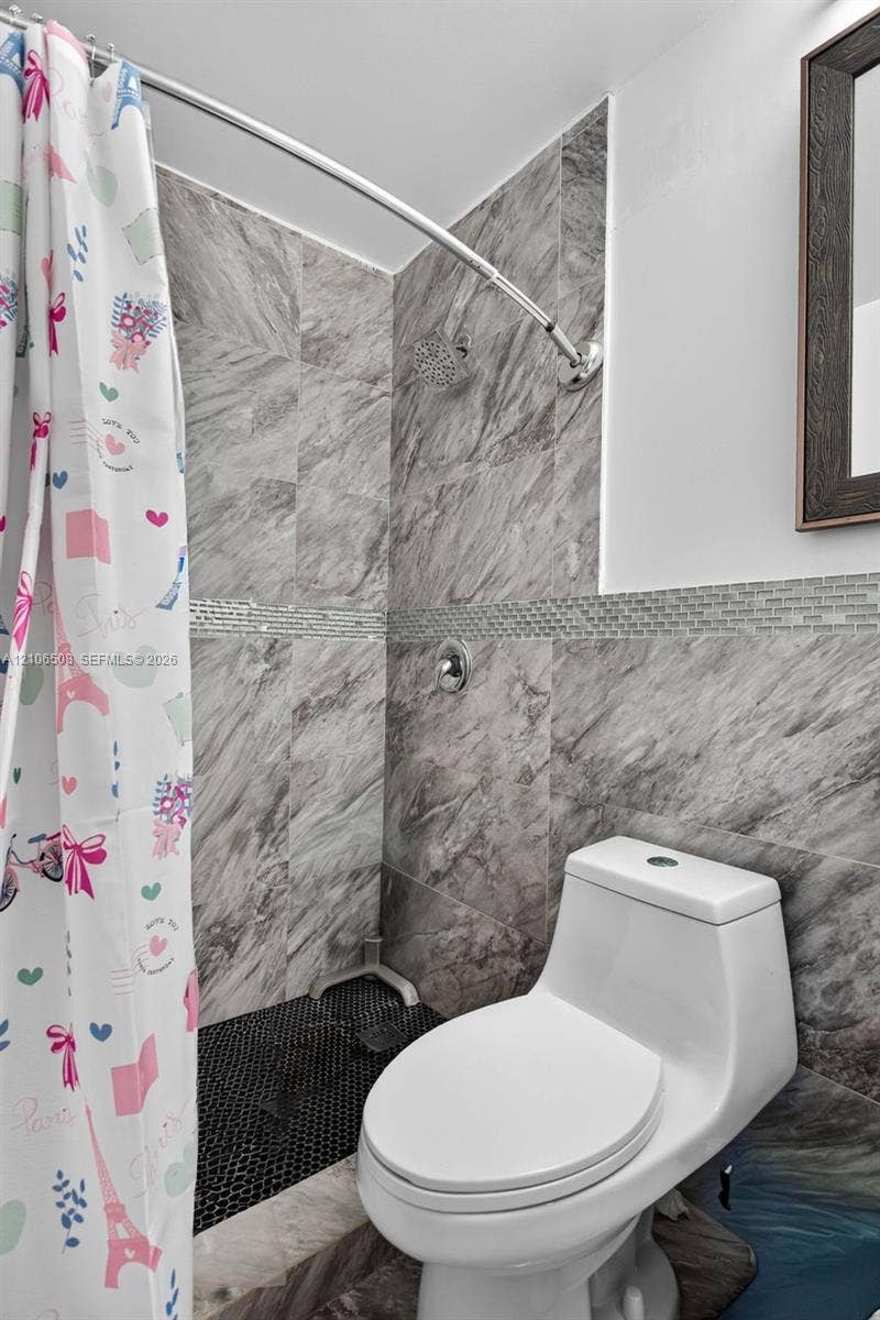 Bathroom featuring full-height large-format stone-patterned wall tile, a mosaic tile accent strip, a black penny tile shower floor, a rainfall shower head, and a dual-flush toilet