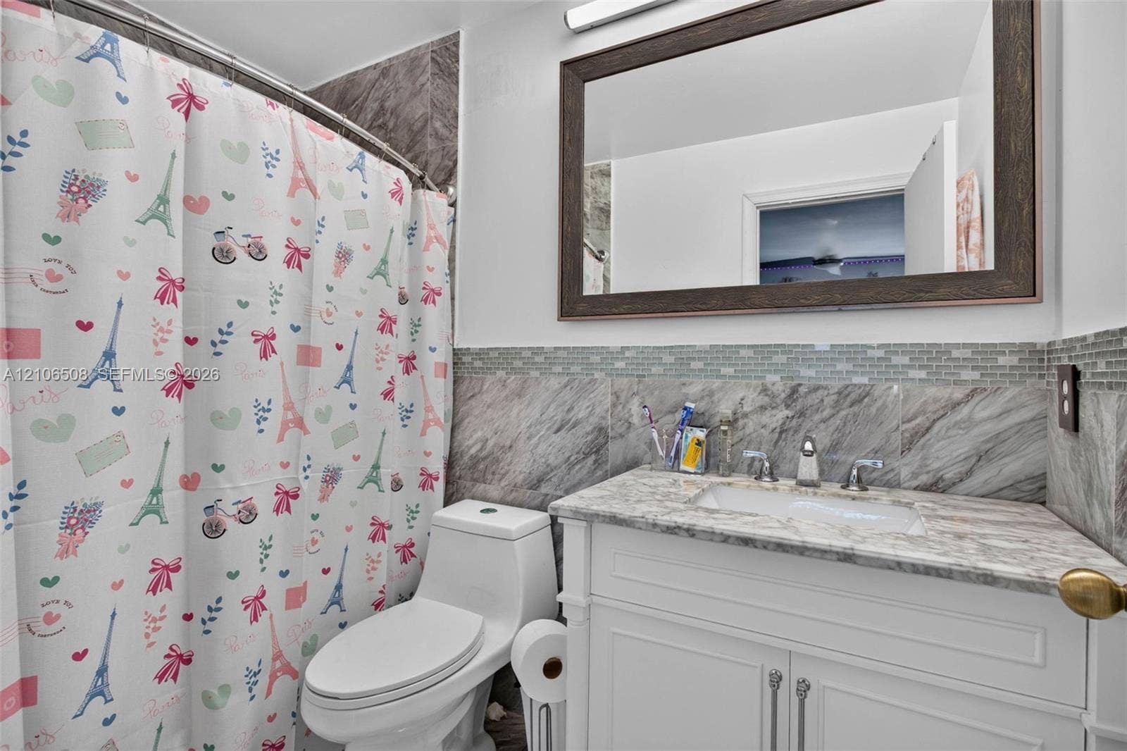 Bathroom featuring white cabinetry, stone-finish vanity countertop with integrated sink, stone-tile backsplash, and wall-mounted framed mirror