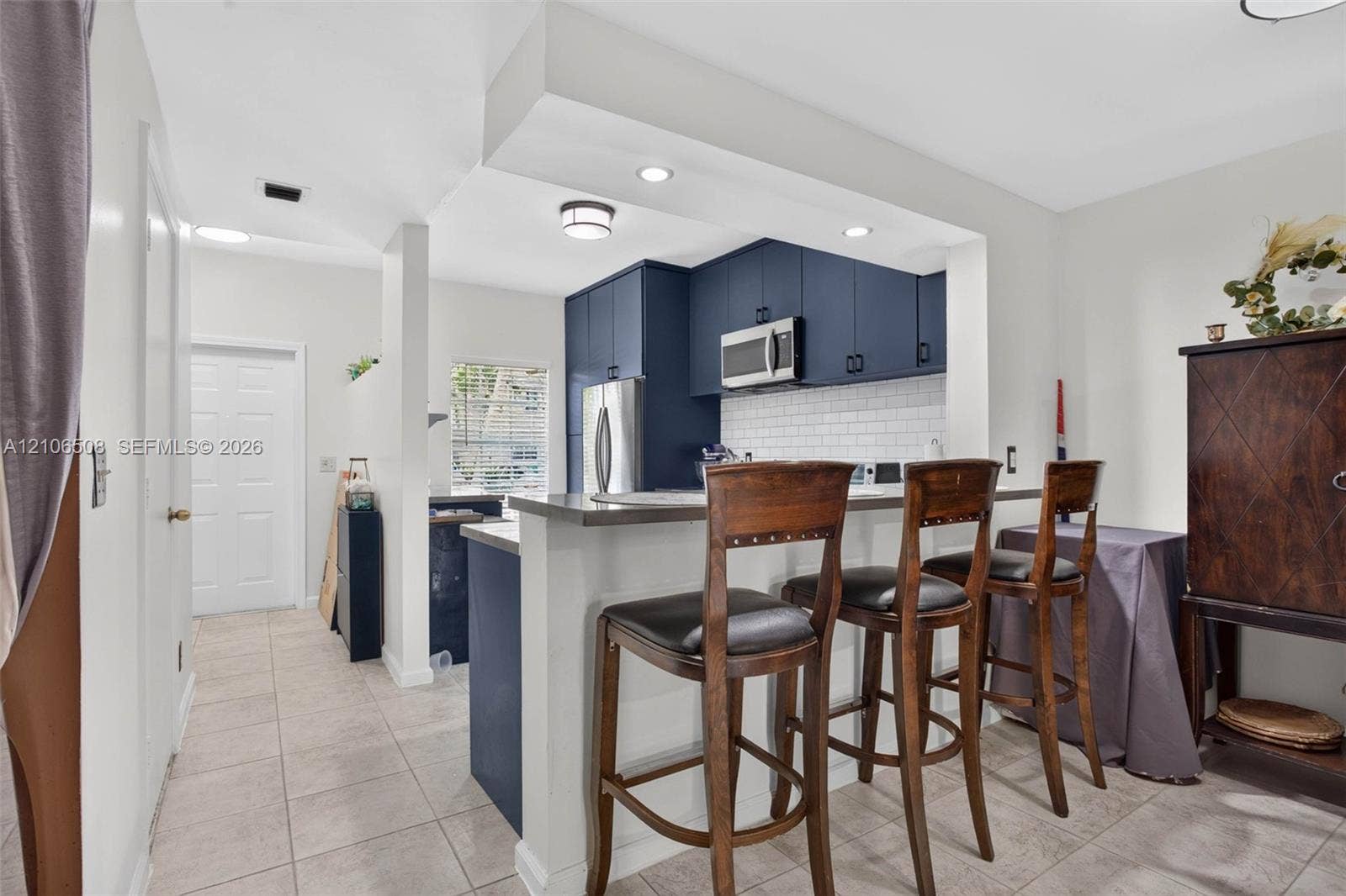 Kitchen featuring navy blue cabinetry, a white subway tile backsplash, a stainless steel over-the-range microwave, and a breakfast bar with a solid surface countertop