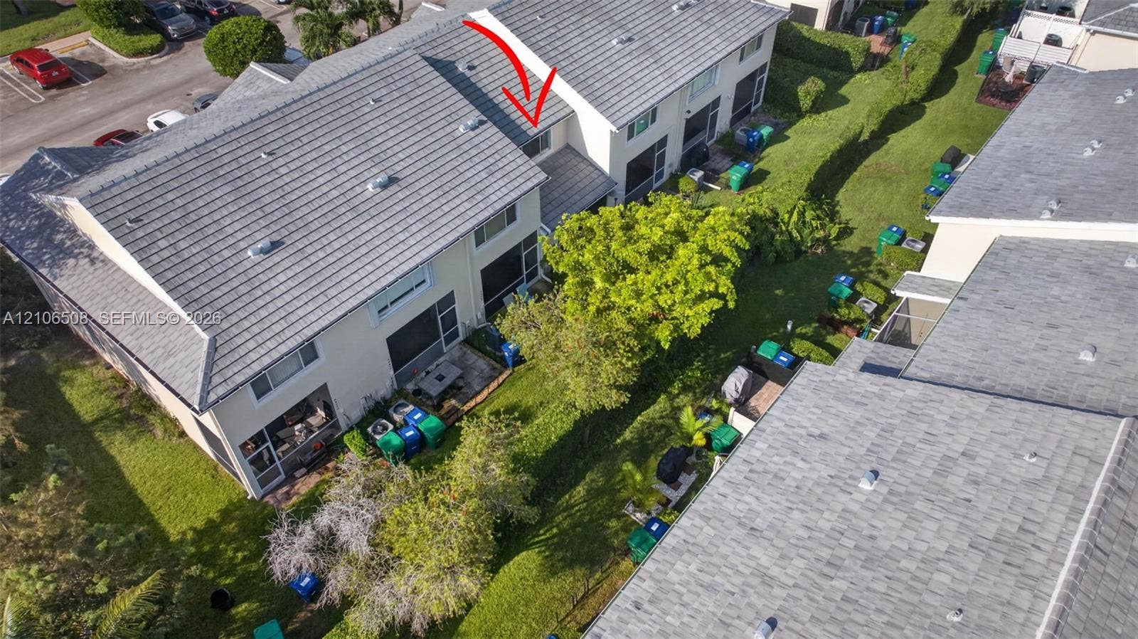 Aerial perspective of a multi-level residential structure featuring a tiled roof, stucco exterior, screened-in rear enclosure, and surrounding landscaped grounds