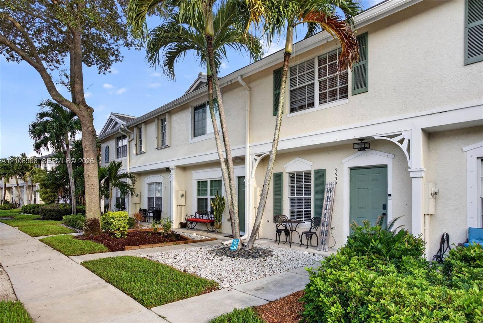 Multi-story exterior featuring light-toned stucco facade, decorative gable trim, shuttered windows, and a paved entry walkway
