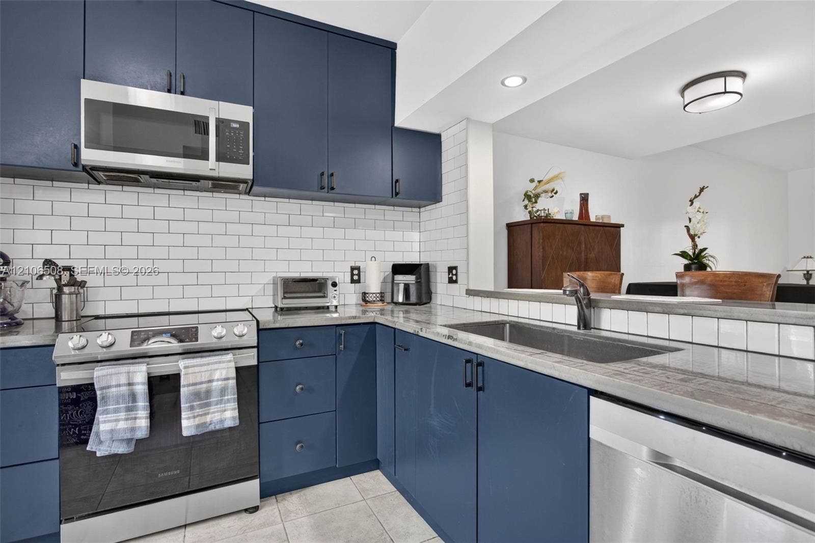 Kitchen featuring navy blue cabinetry, white subway tile backsplash, solid-surface countertops, stainless steel appliances, and a stainless steel undermount sink