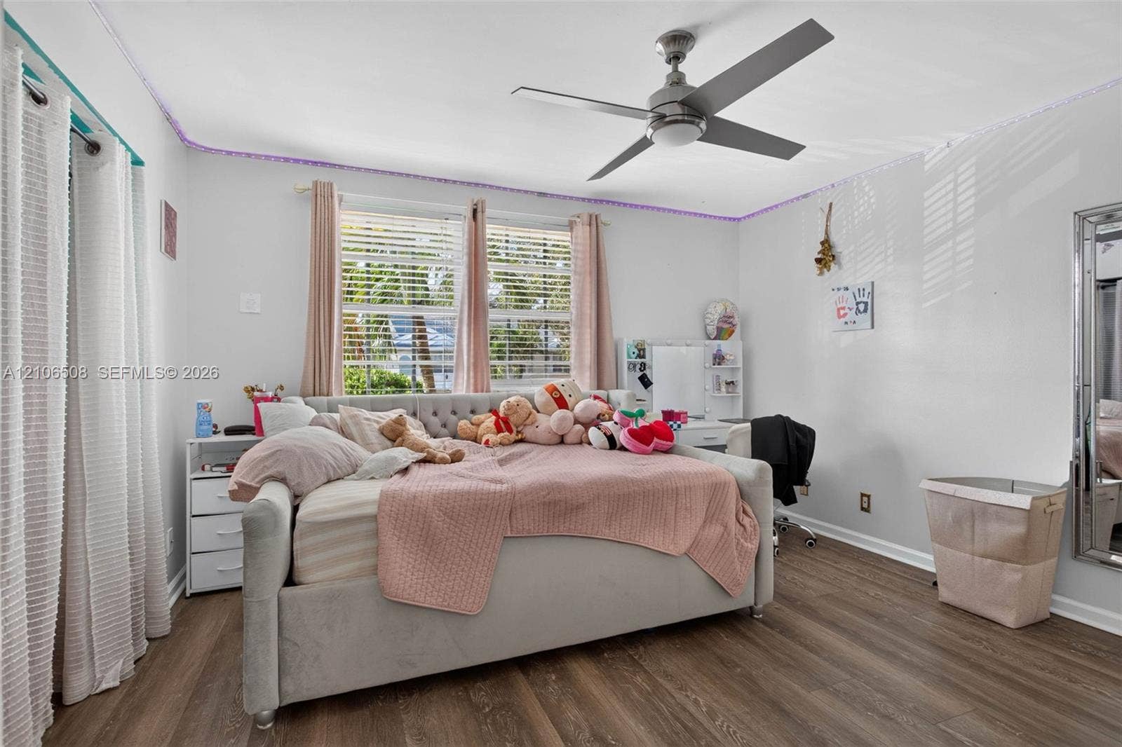 Wood-finish flooring, dual windows with horizontal blinds, and a central ceiling fan with integrated lighting