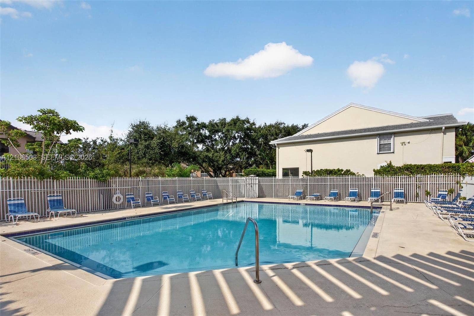 In-ground swimming pool featuring a concrete deck, metal perimeter fencing, and stainless steel pool ladder
