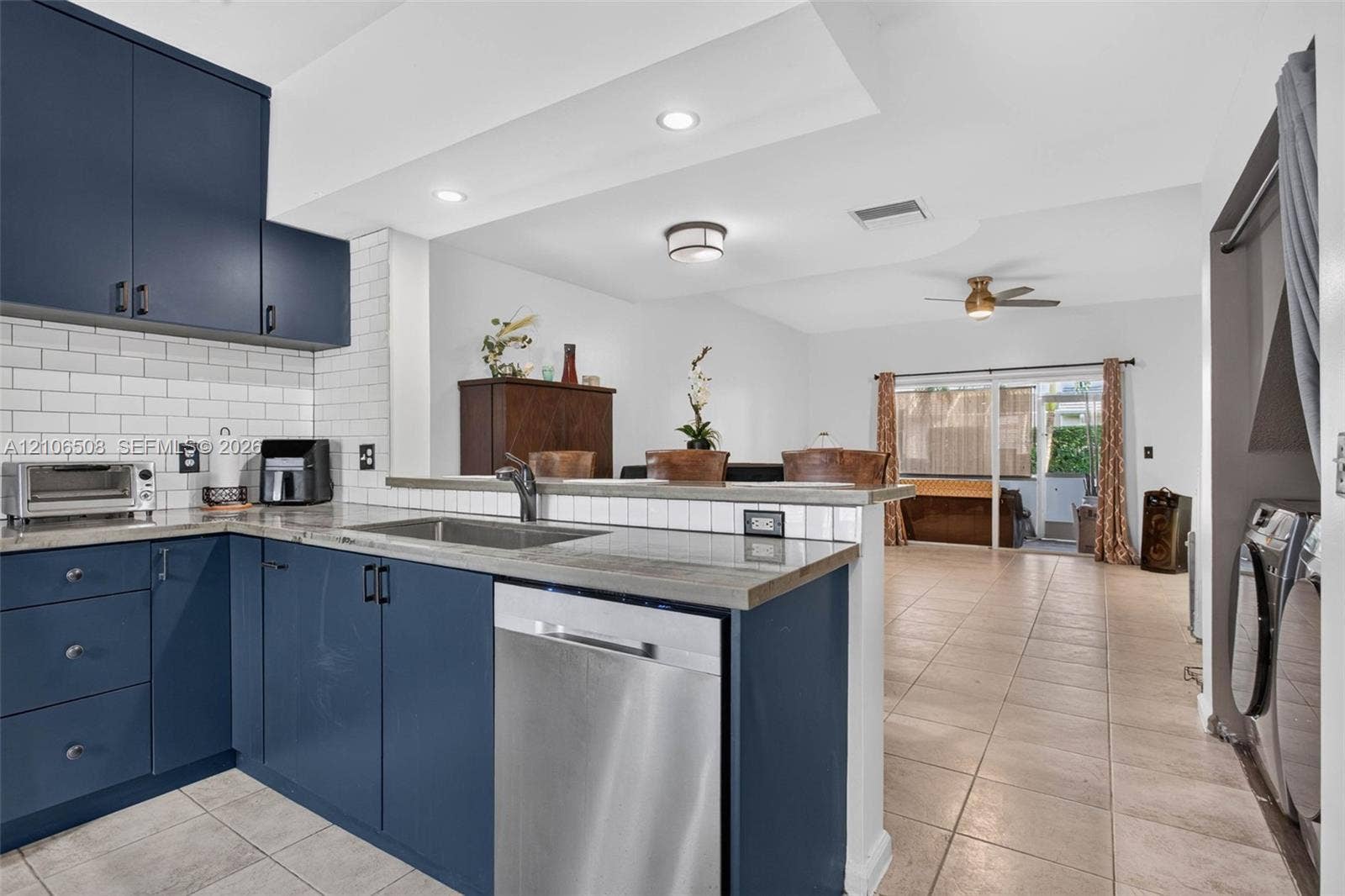 Kitchen featuring navy cabinetry, stone-surface countertops, white subway tile backsplash, stainless steel dishwasher, and tile flooring